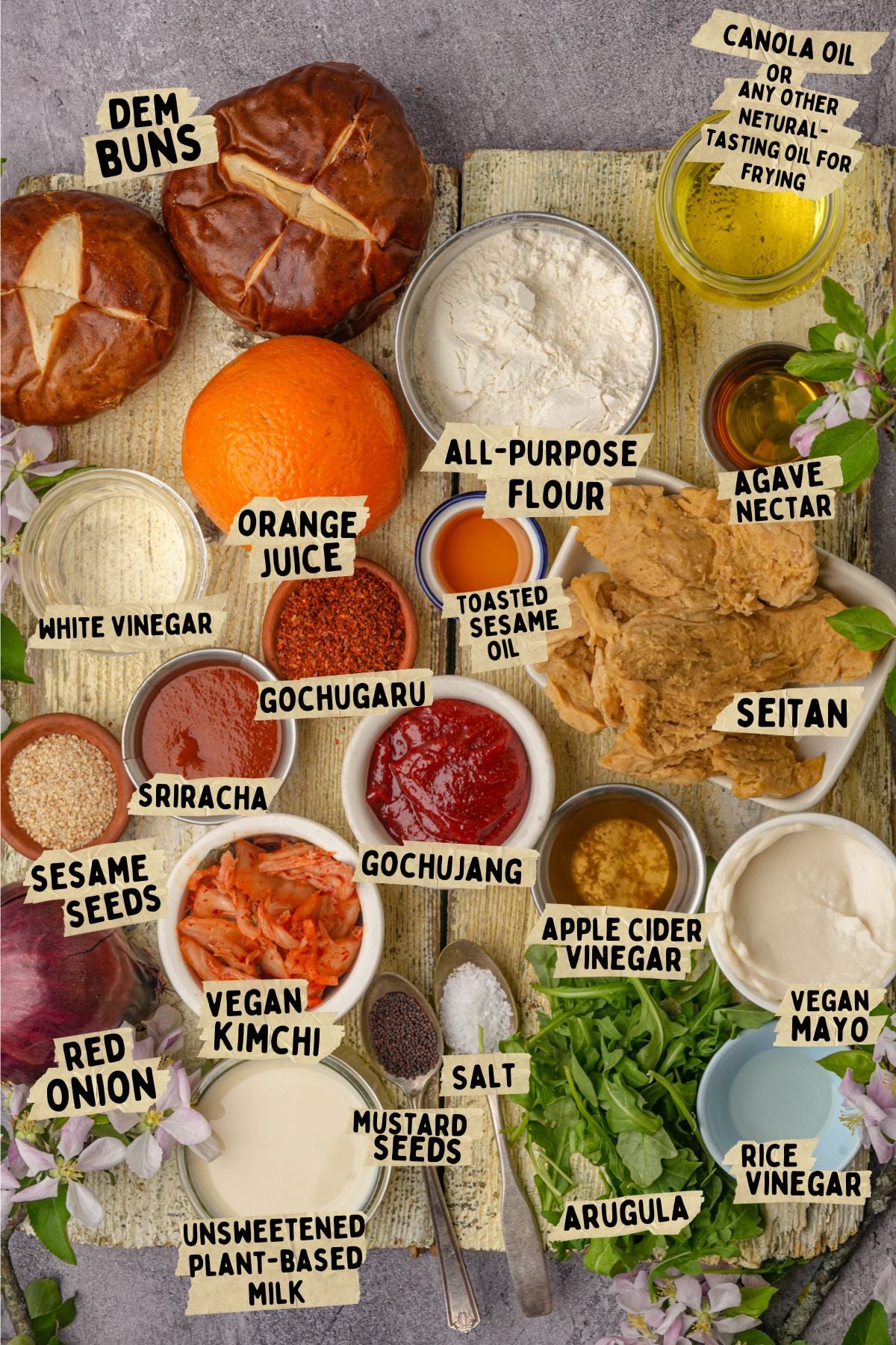 Labeled ingredients for a vegan gochujang seitan sandwich, including buns, flour, orange juice, seitan, vegan mayo, kimchi, sriracha, gochujang, spices, oils, arugula, vinegar, salt, and agave nectar.