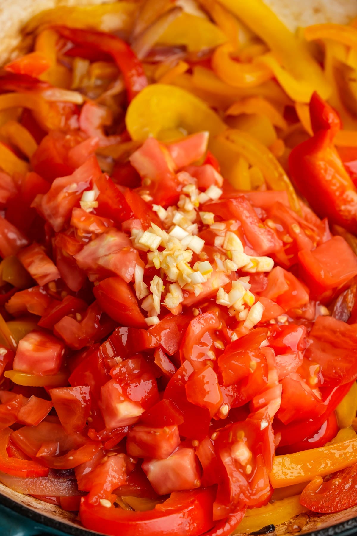 Chopped tomatoes, minced garlic, and sliced peppers in a pan, cooking down to become peperonata.