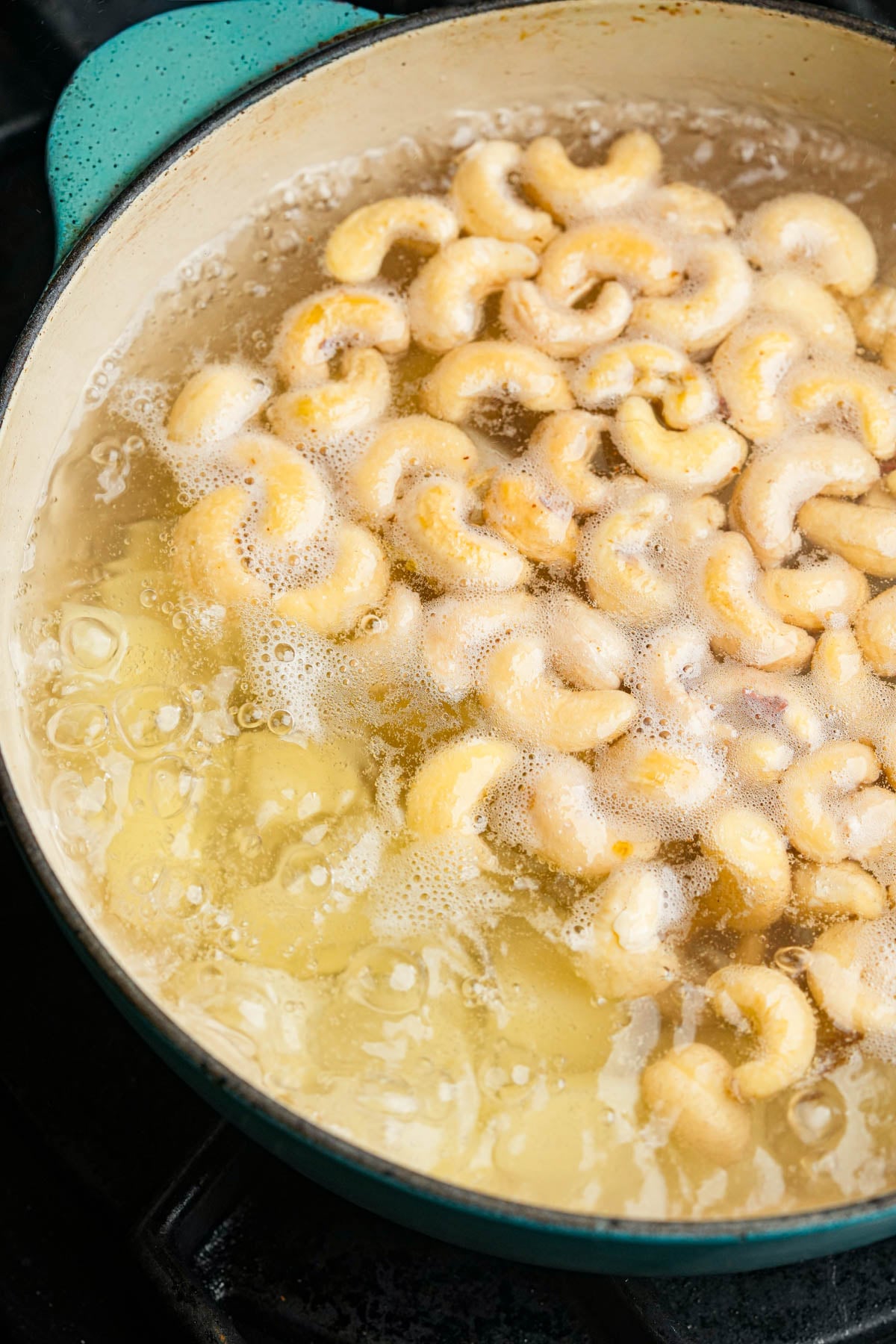 Cashews and potatoes boiling in a pot of water on a stovetop.