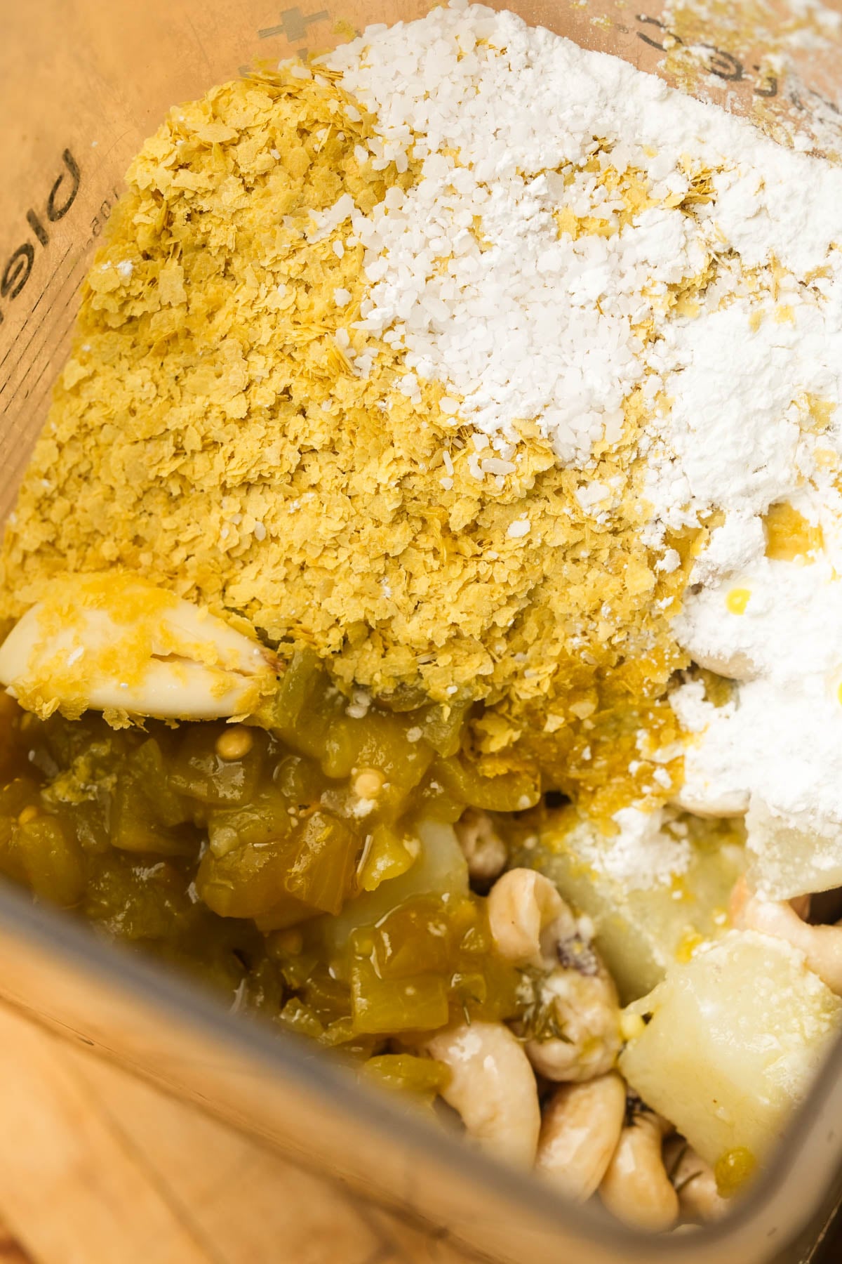 A blender containing cooked potatoes, cashews, green chiles, nutritional yeast, and tapioca starch, ready to be blended for a vegan queso recipe.