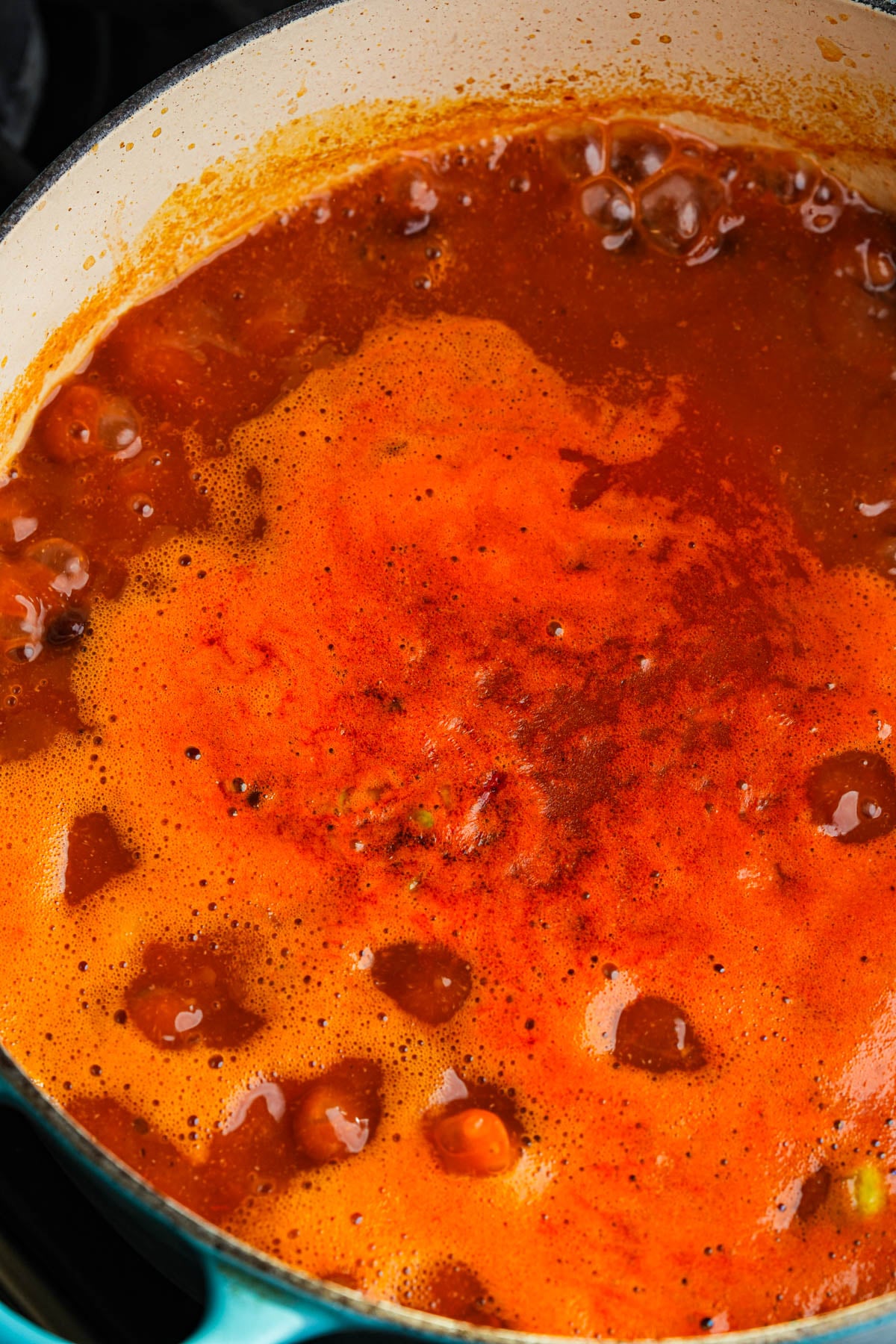 A close-up of a simmering pot of vegan taco soup with bubbles forming on the surface, viewed from above in a teal enameled cast iron pot.