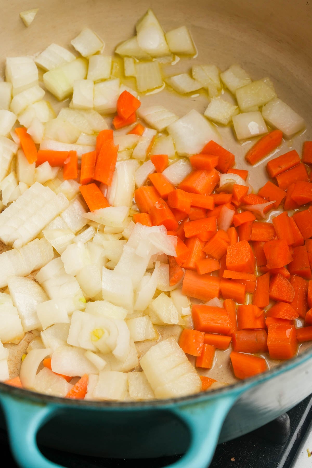 Diced onions and carrots are sautéing in oil in a large light green pot on a stovetop.