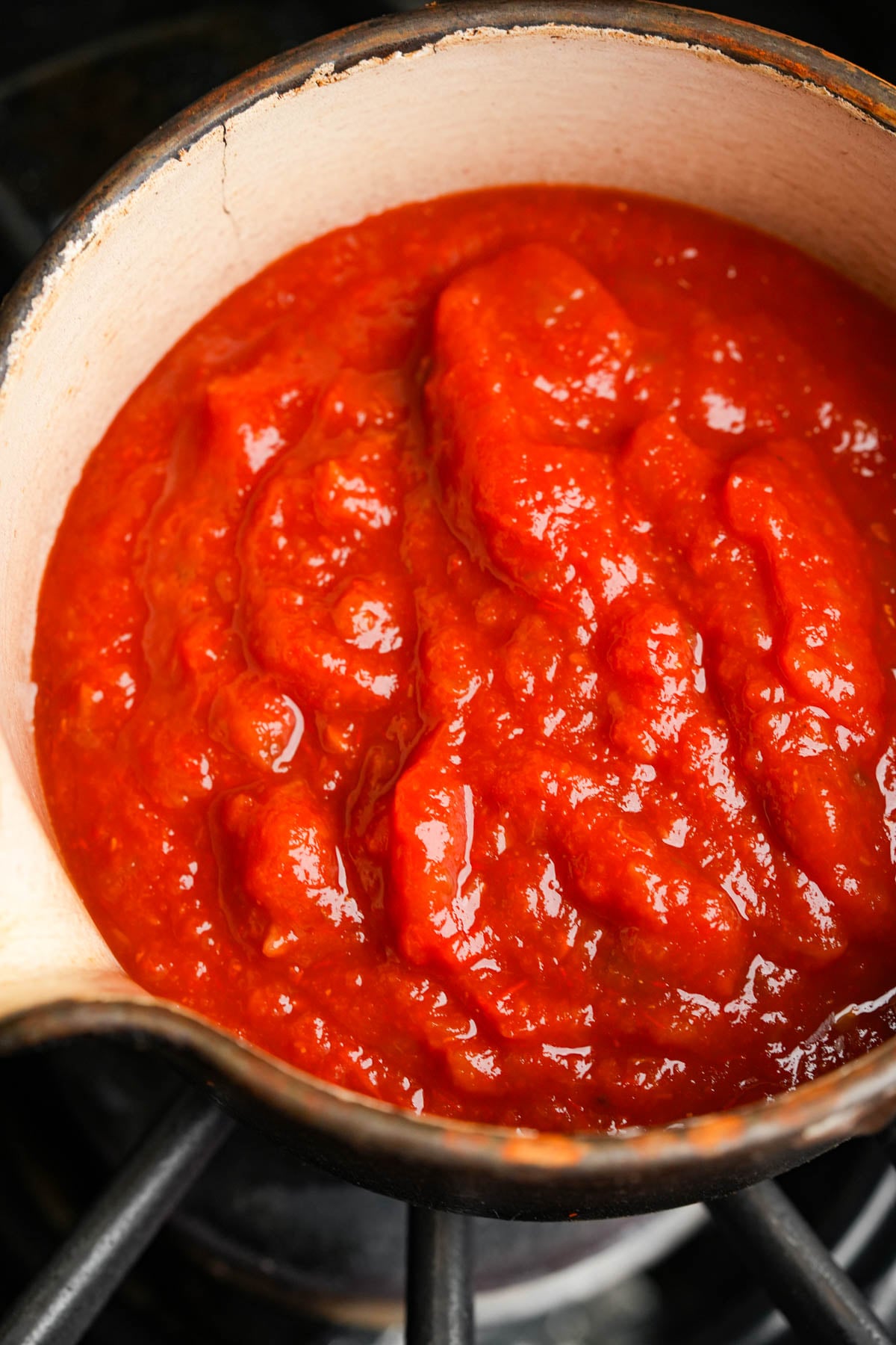 Thick salsa rojo simmering in a white pot on a stovetop.