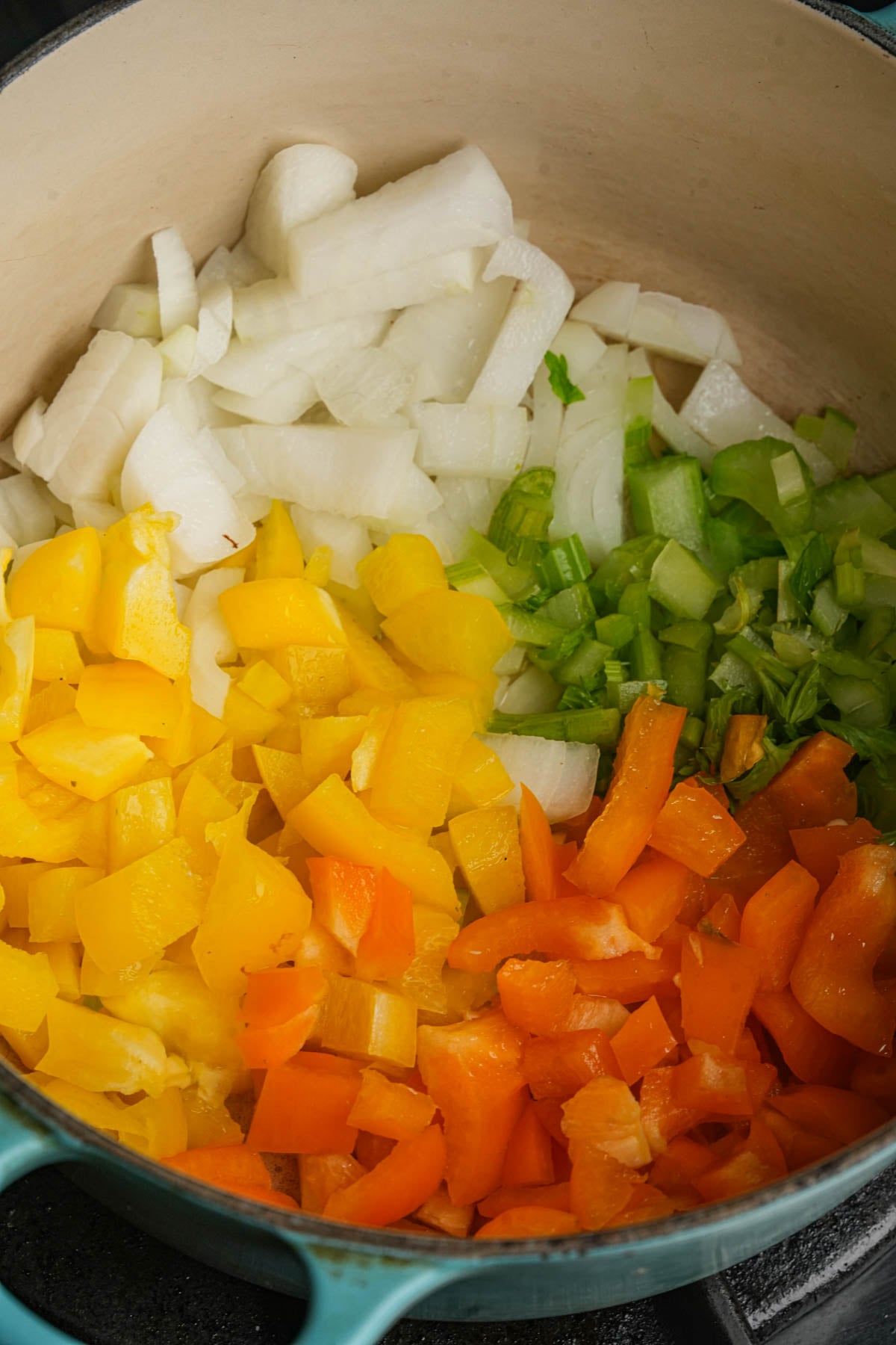 Chopped yellow bell pepper, orange bell pepper, celery, and onion arranged in sections inside a large pot, ready for cooking.
