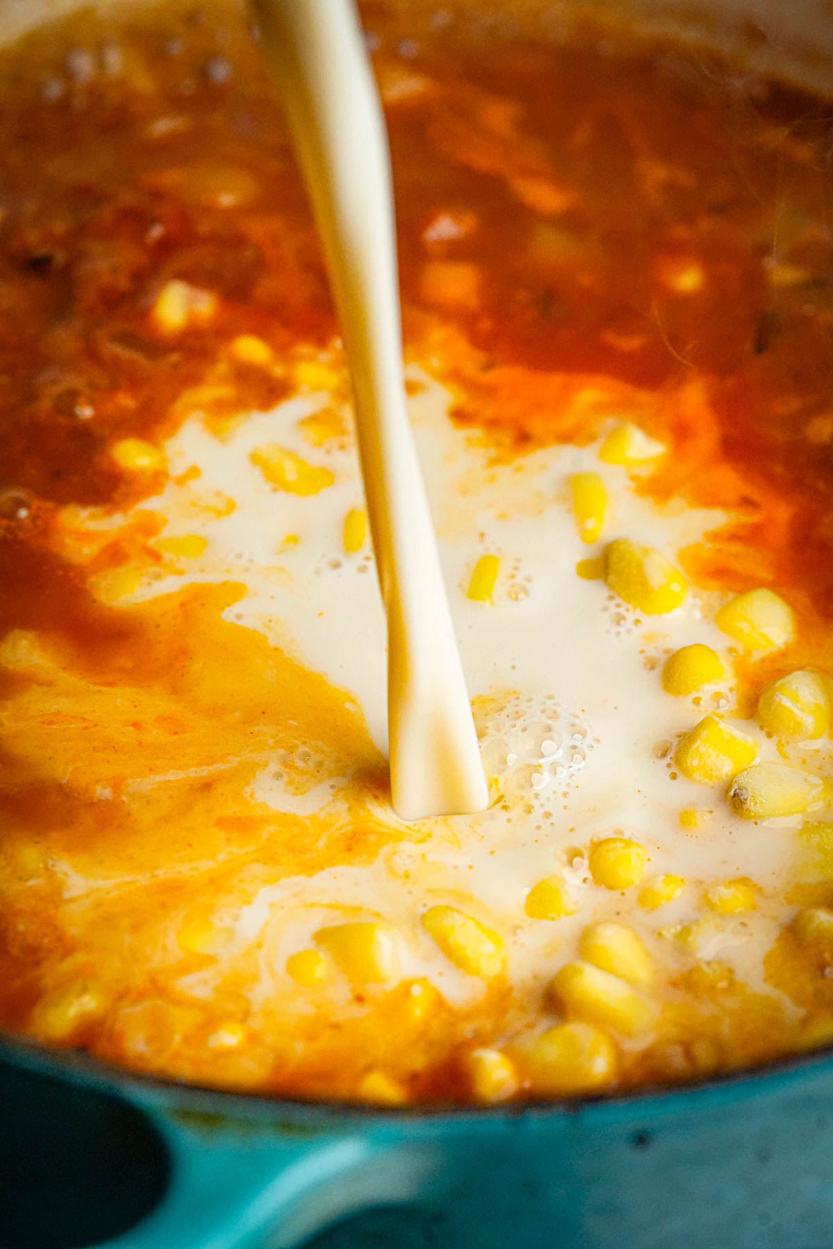 A stream of vegan milk is being poured into a pot of vegan corn chowder.