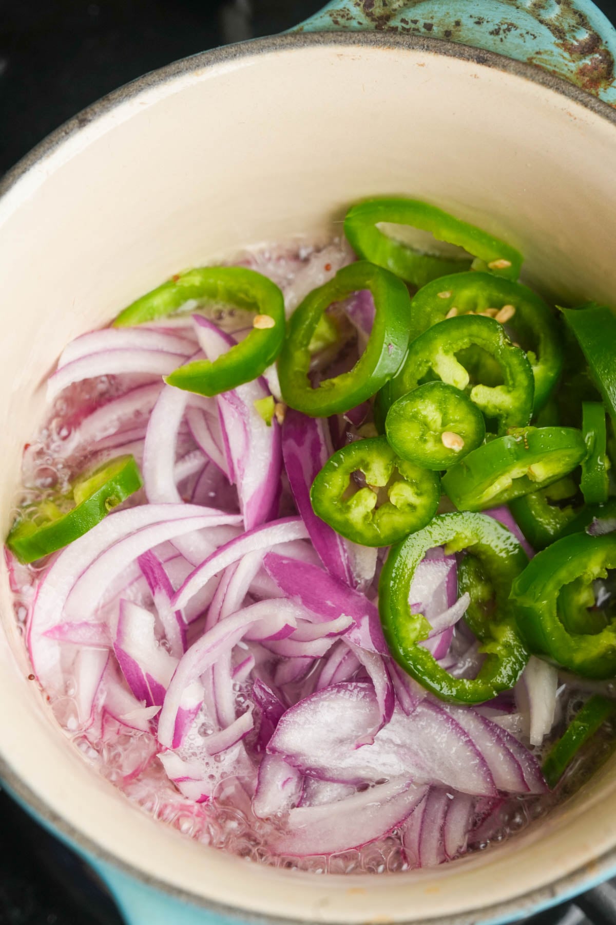 Sliced red onions and green jalapeños cooking in a pot with bubbling oil-the perfect base for a flavorful Vegan Frito Pie Casserole.