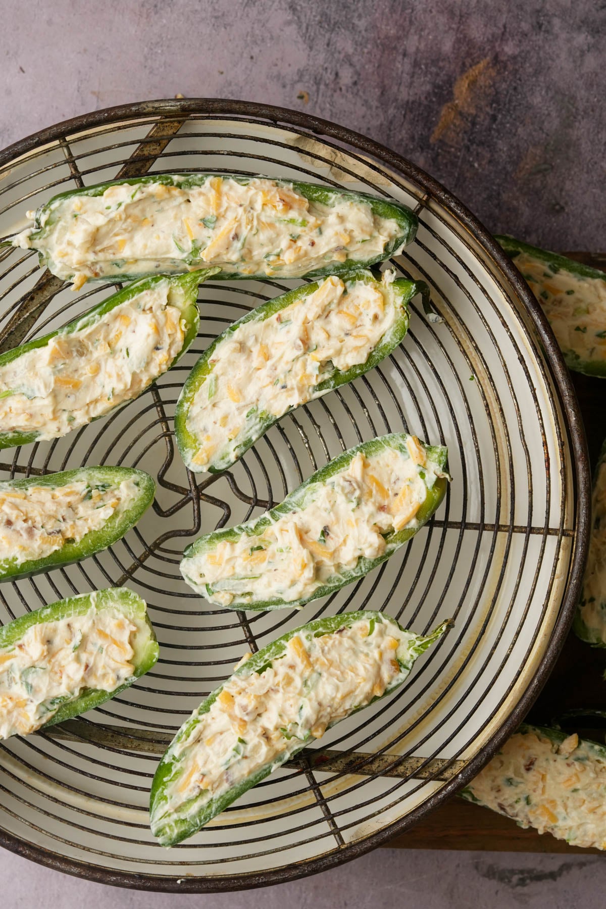 Halved jalapeños filled with a creamy cheese mixture are arranged on a round wire rack over a lined baking sheet, ready to be fried into vegan jalapeno poppers.