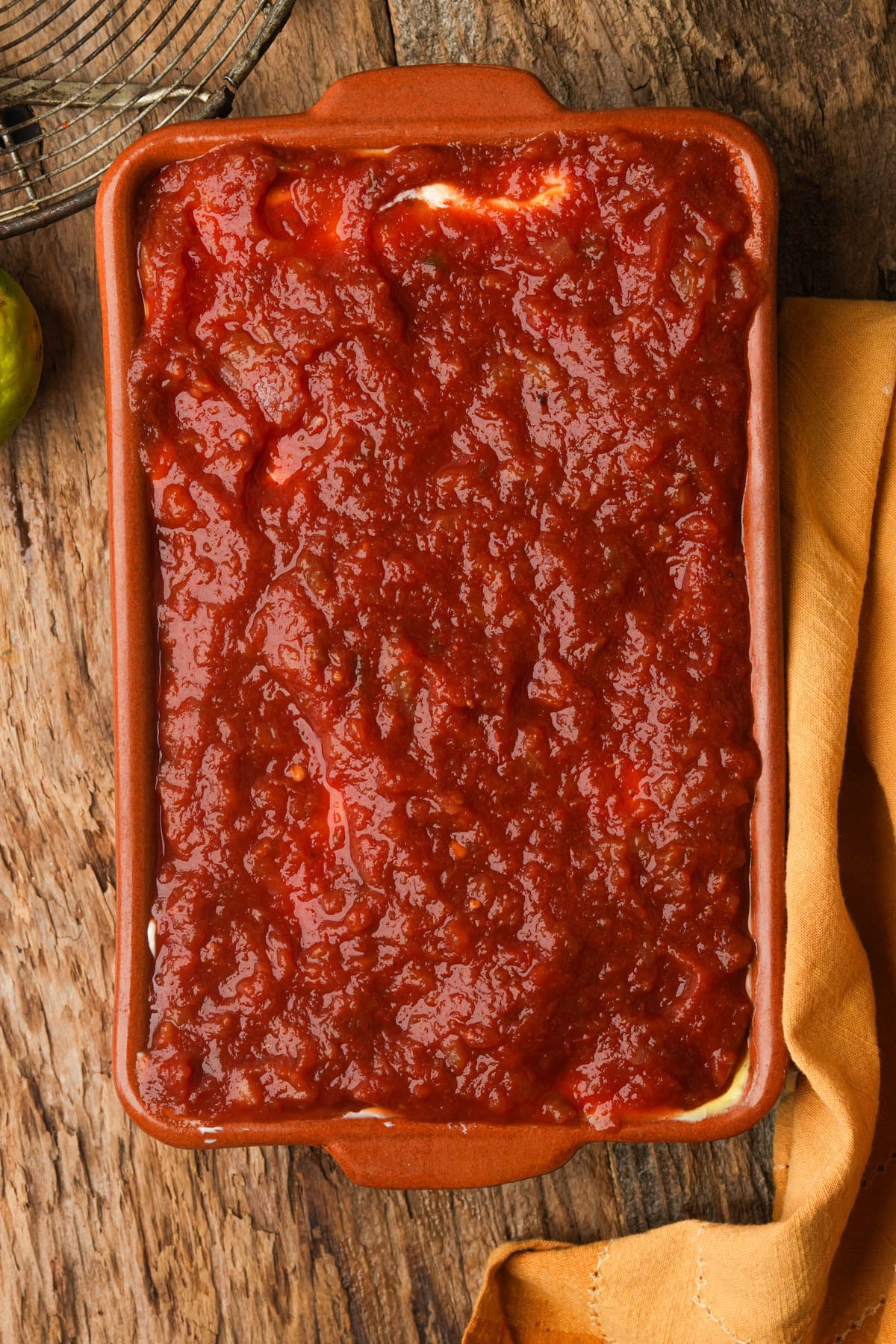 A rectangular baking dish filled with vegan seven-layer dip, topped with a thick layer of salsa rojo.
