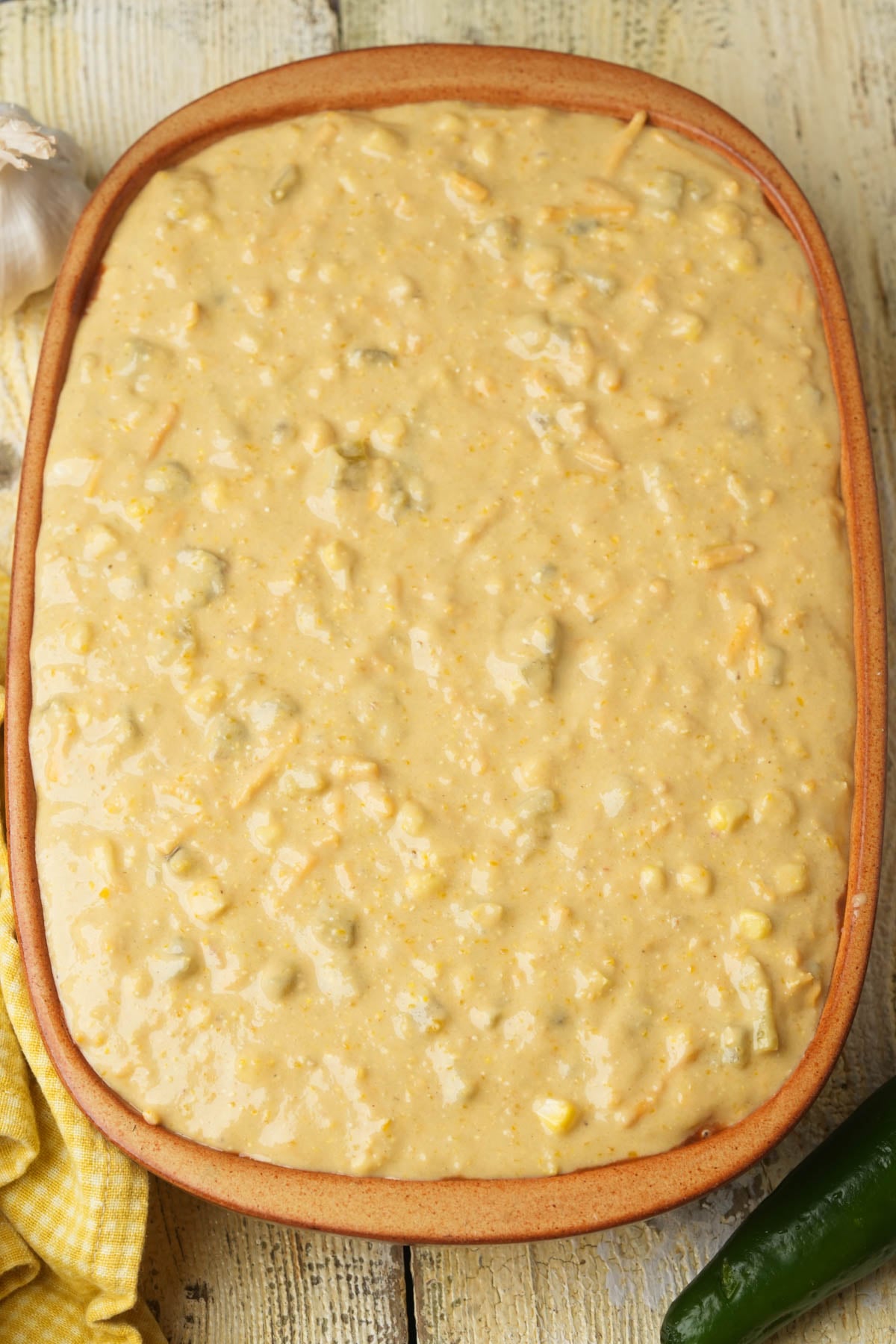 A rectangular baking dish filled with an uncooked vegan tamale pie sitting on a light wooden surface.