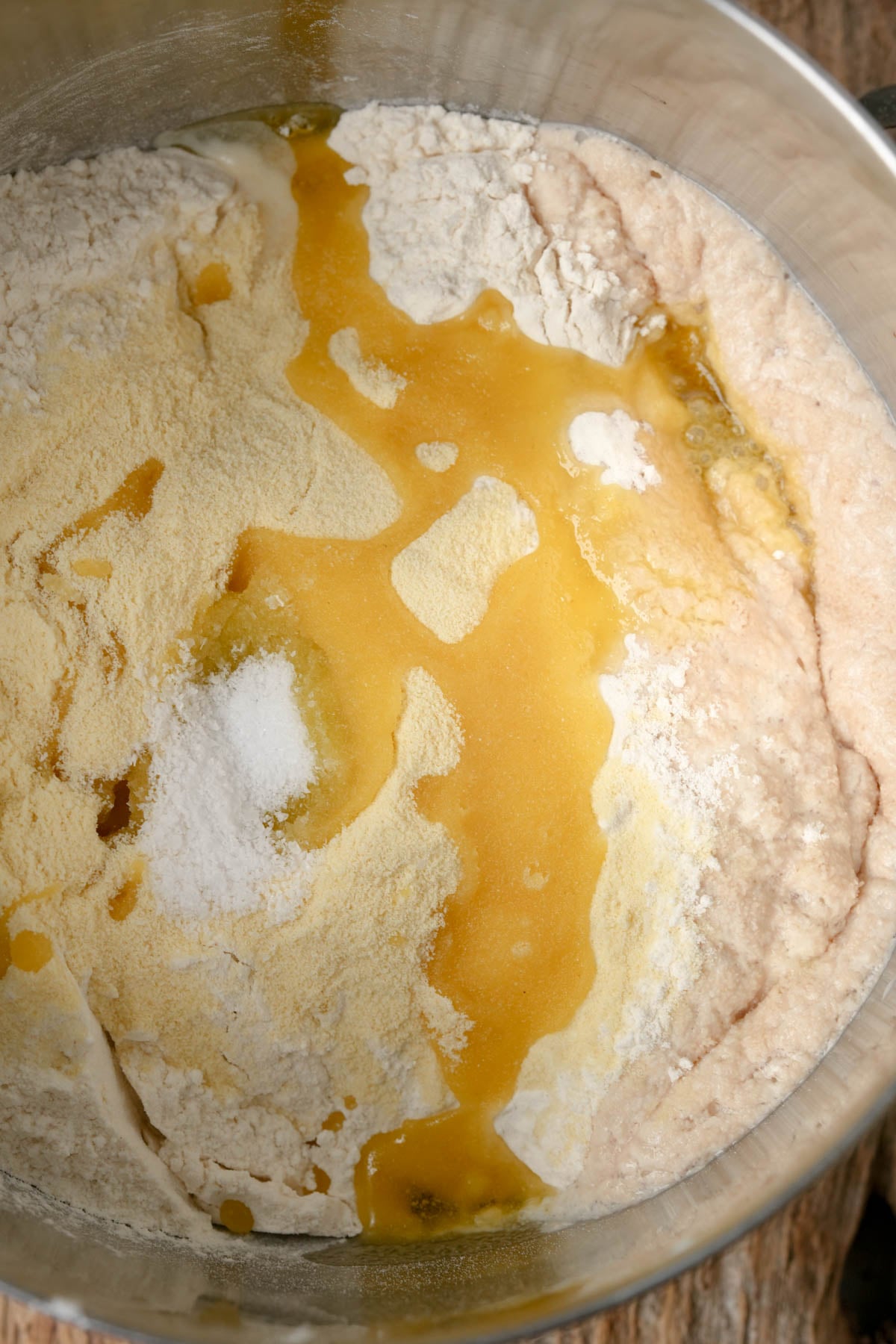 Flour, semolina, and baking ingredients in a metal mixing bowl with liquid being poured in, ready to be mixed for baking.