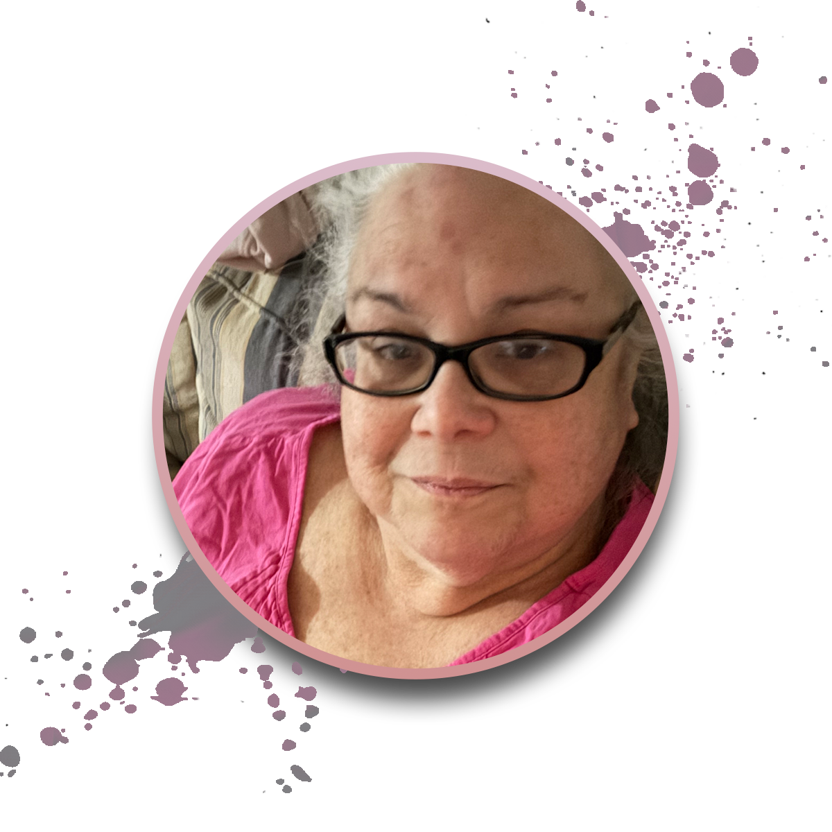 An older woman with glasses and gray hair, wearing a pink top, smiles slightly. The photo is framed in a pink circle with purple paint splatter accents on a white background.