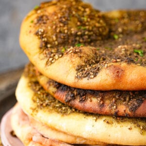 A stack of Manakeesh topped with zaatar seasoning, showing golden-brown, baked surfaces with specks of herbs and sesame seeds.