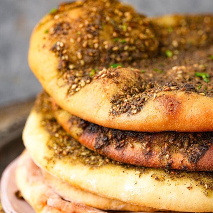 A stack of Manakeesh topped with zaatar seasoning, showing golden-brown, baked surfaces with specks of herbs and sesame seeds.