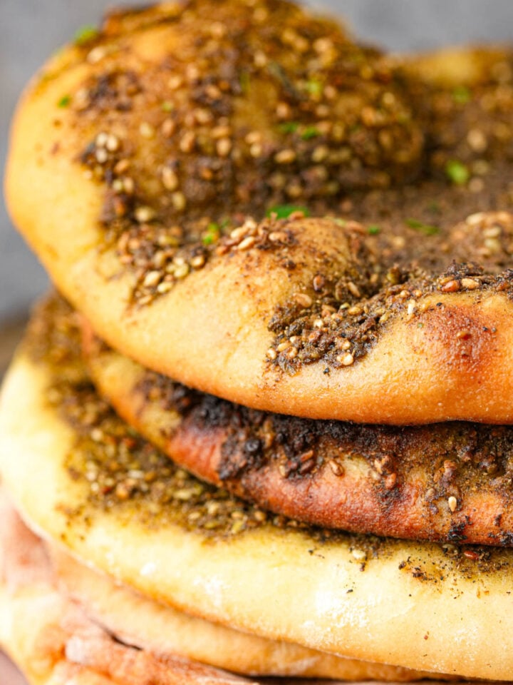A stack of Manakeesh topped with zaatar seasoning, showing golden-brown, baked surfaces with specks of herbs and sesame seeds.