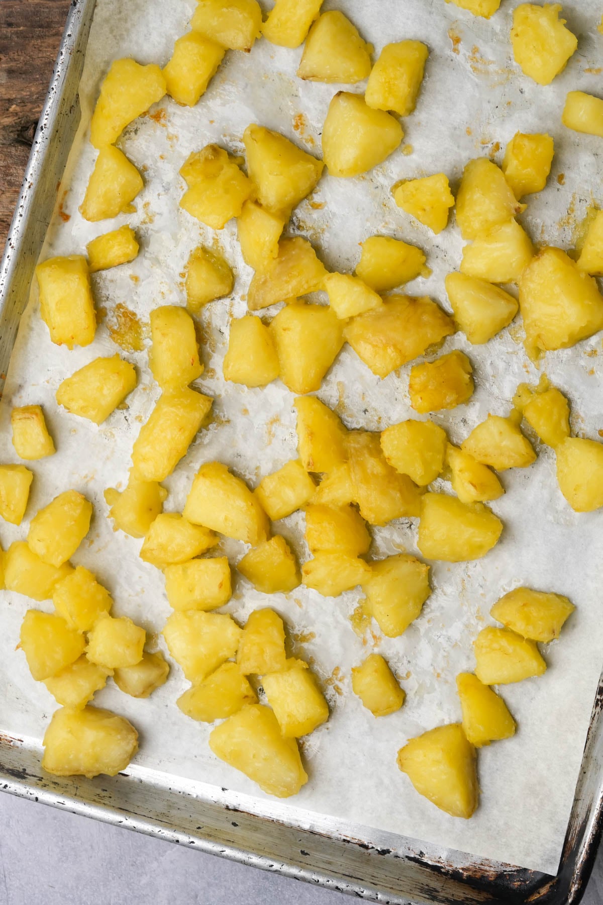A baking sheet lined with parchment paper holds scattered, golden-yellow roasted potato chunks. The potatoes appear crispy on the outside and soft inside, spaced out across the tray.