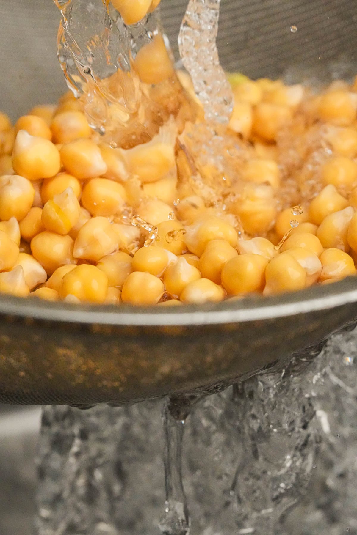 Water is being poured over a colander filled with chickpeas, rinsing them thoroughly.