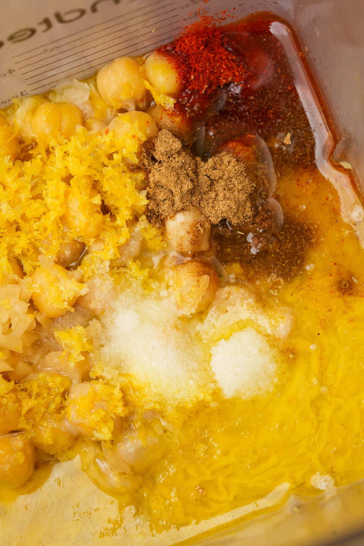 Chickpeas, olive oil, lemon zest, spices, and garlic are placed together in a blender, ready to be blended into lemon hummus.