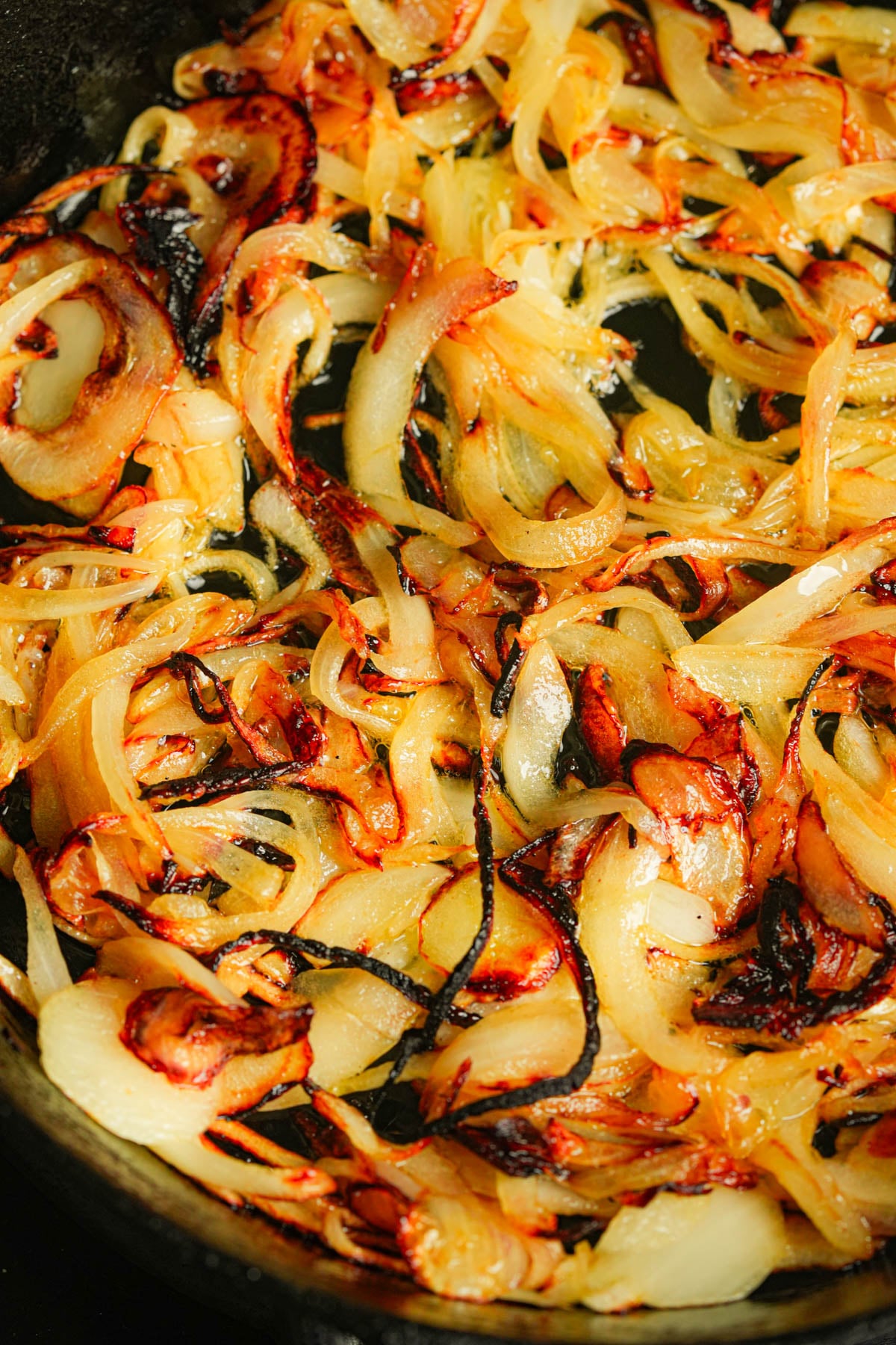 Sliced onions frying, with some pieces darker, crispy edges, are shown cooking in a pan.