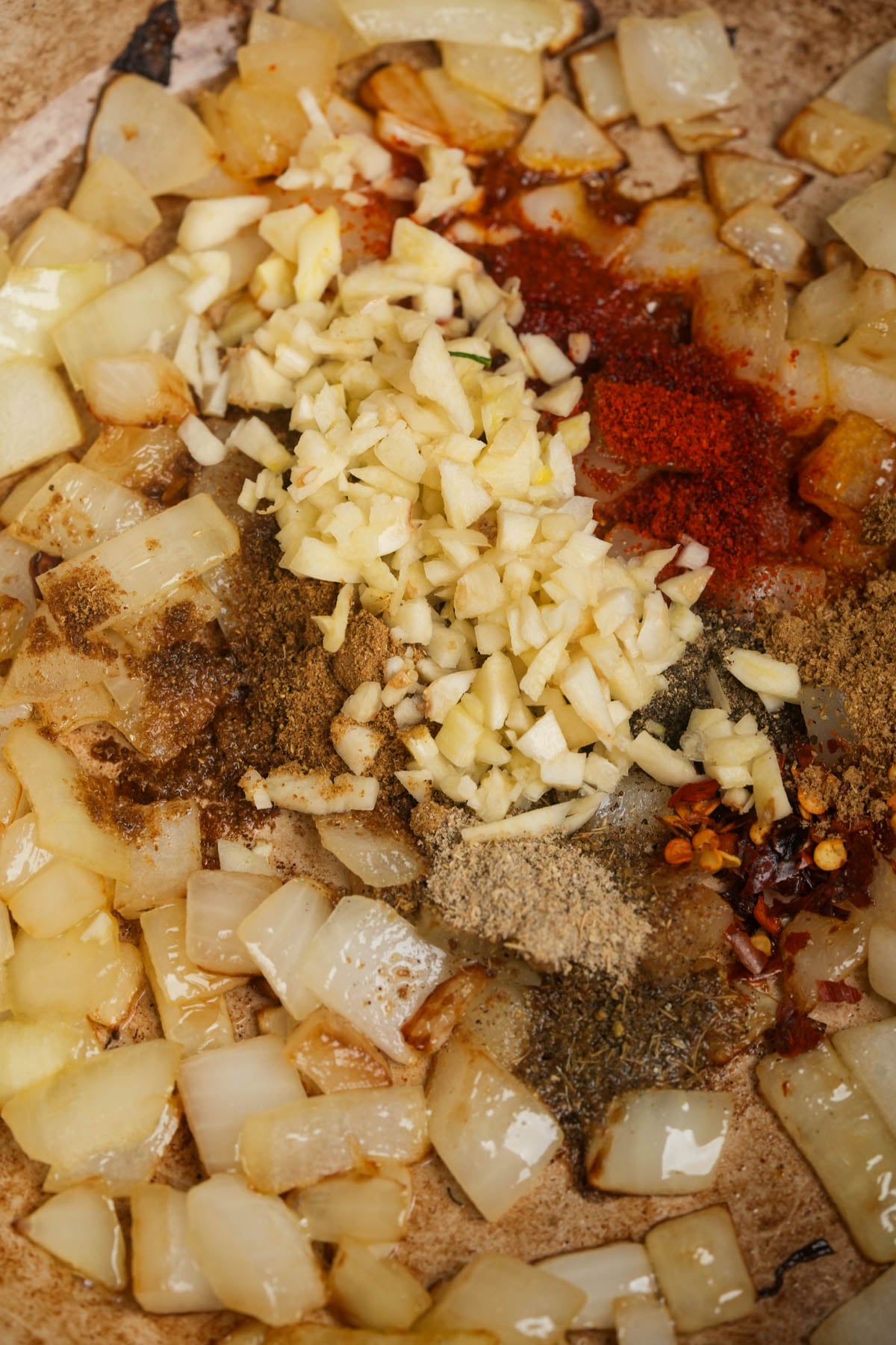 Chopped onions sautéed in a pan with minced garlic, ground spices, and red chili flakes.