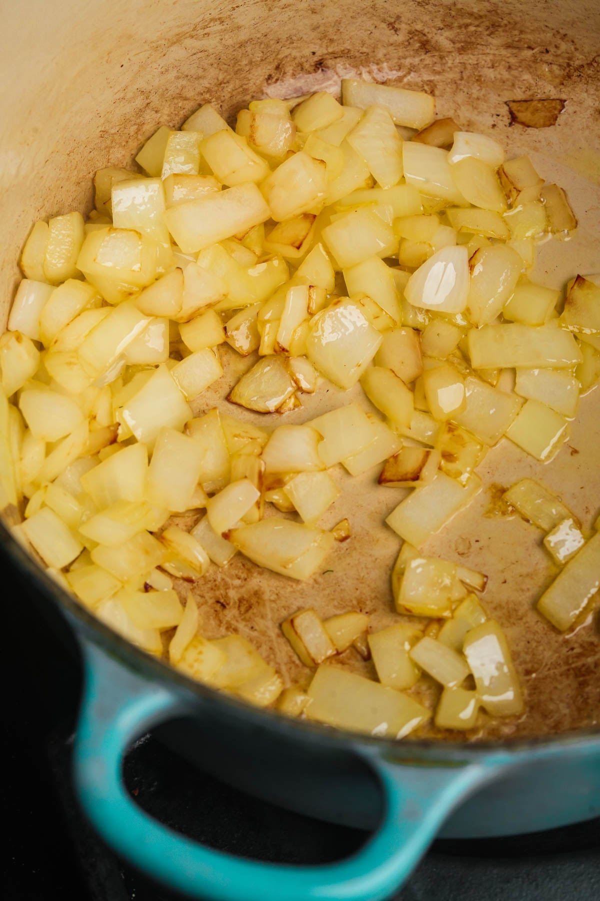 Diced onions sautéing in oil inside a blue pot, some pieces turning golden brown, indicating the beginning stage of cooking.