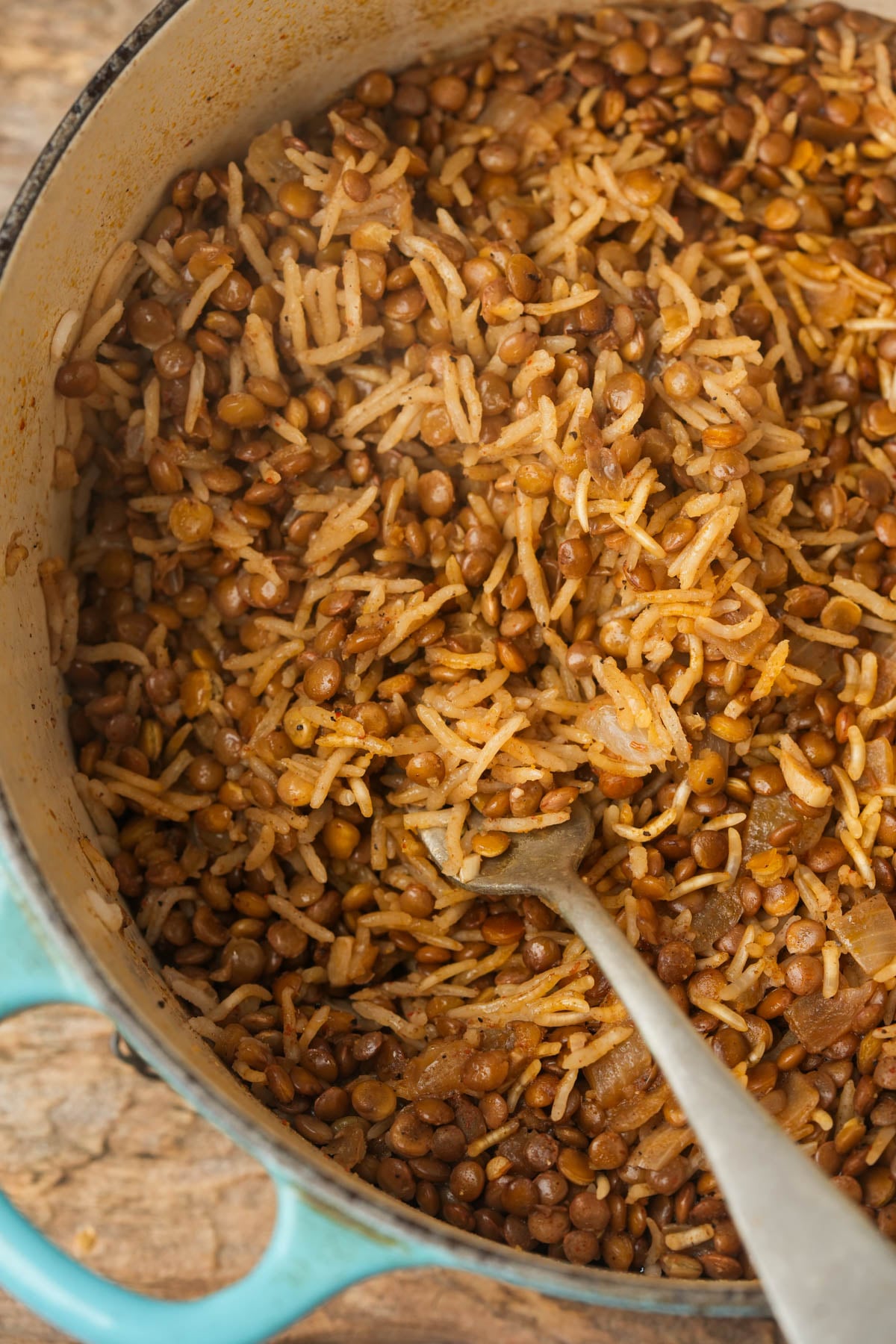 Mujadara in a pot, with a metal spoon resting inside. The dish appears seasoned and hearty, with visible grains and lentils.