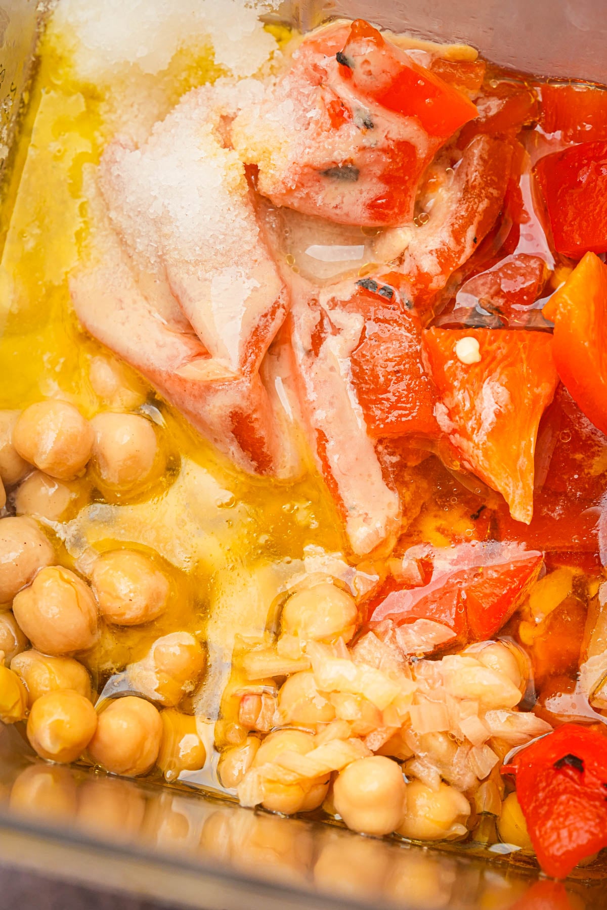 A blender full og chickpeas, roasted red peppers, olive oil, salt, and chopped garlic, ready to be blended into roasted red pepper hummus.