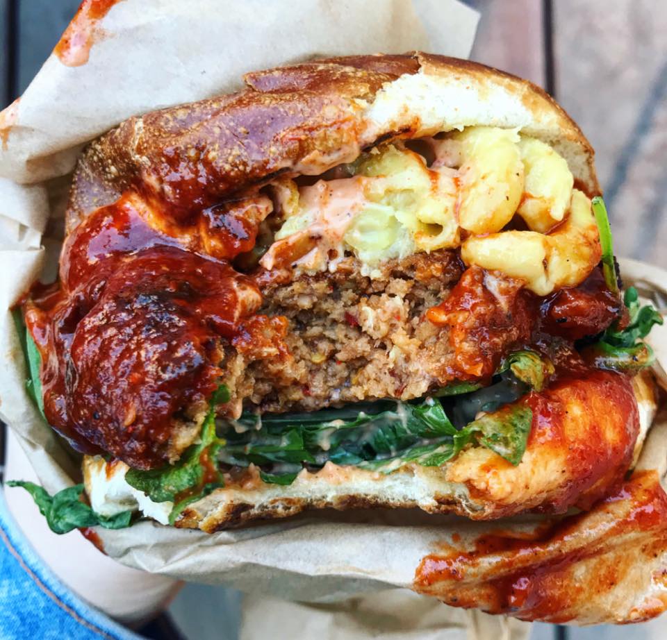 Cross-section of the seitan burger showing the patty, mac and cheese, and BBQ sauce, held in wax paper