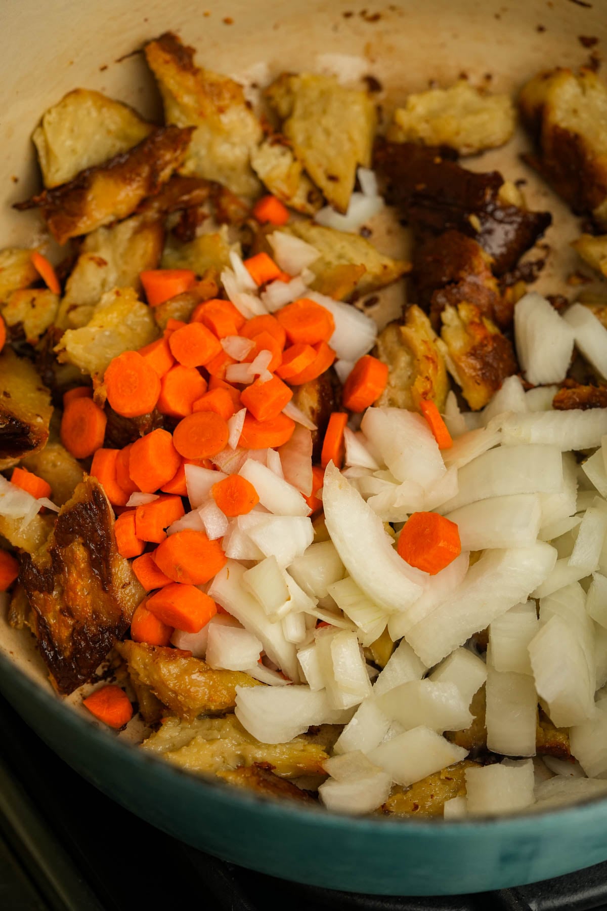 Diced onions and sliced carrots are being sautéed with browned chunks of seitan in a pan.