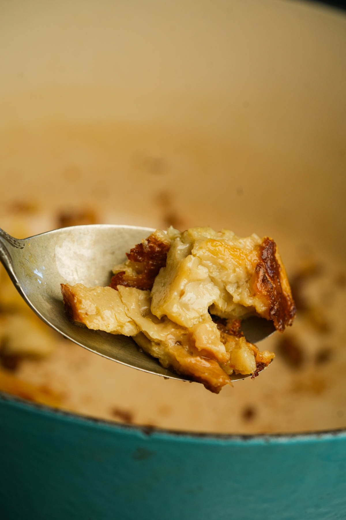 A spoon holding a bite of golden, crusty seitan above a blue pot, with more seitan pieces inside the pot in the background.