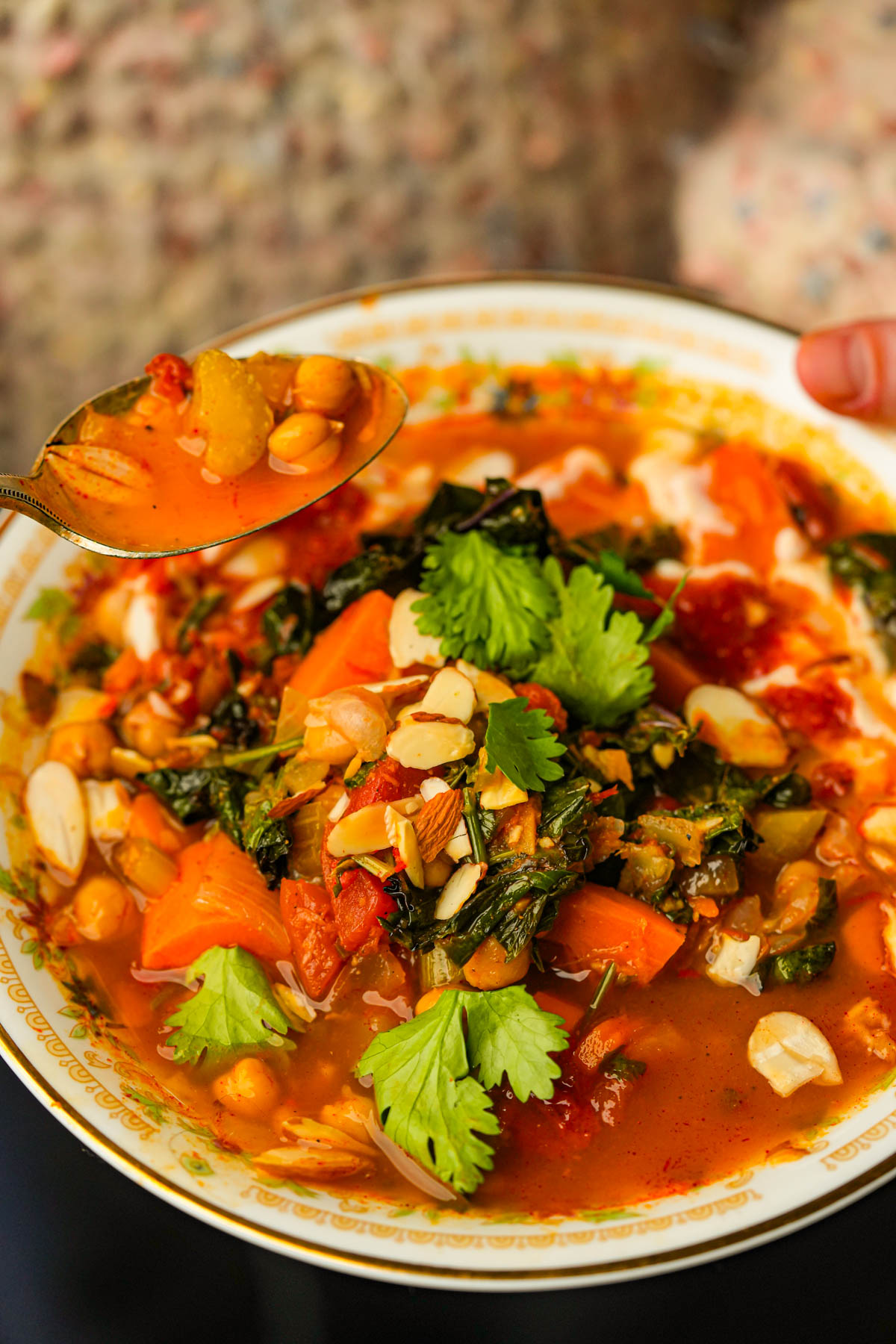 A bowl of Moroccan sweet potato soup with chickpeas, greens, chopped nuts, and fresh cilantro, with a spoonful lifted above the bowl.