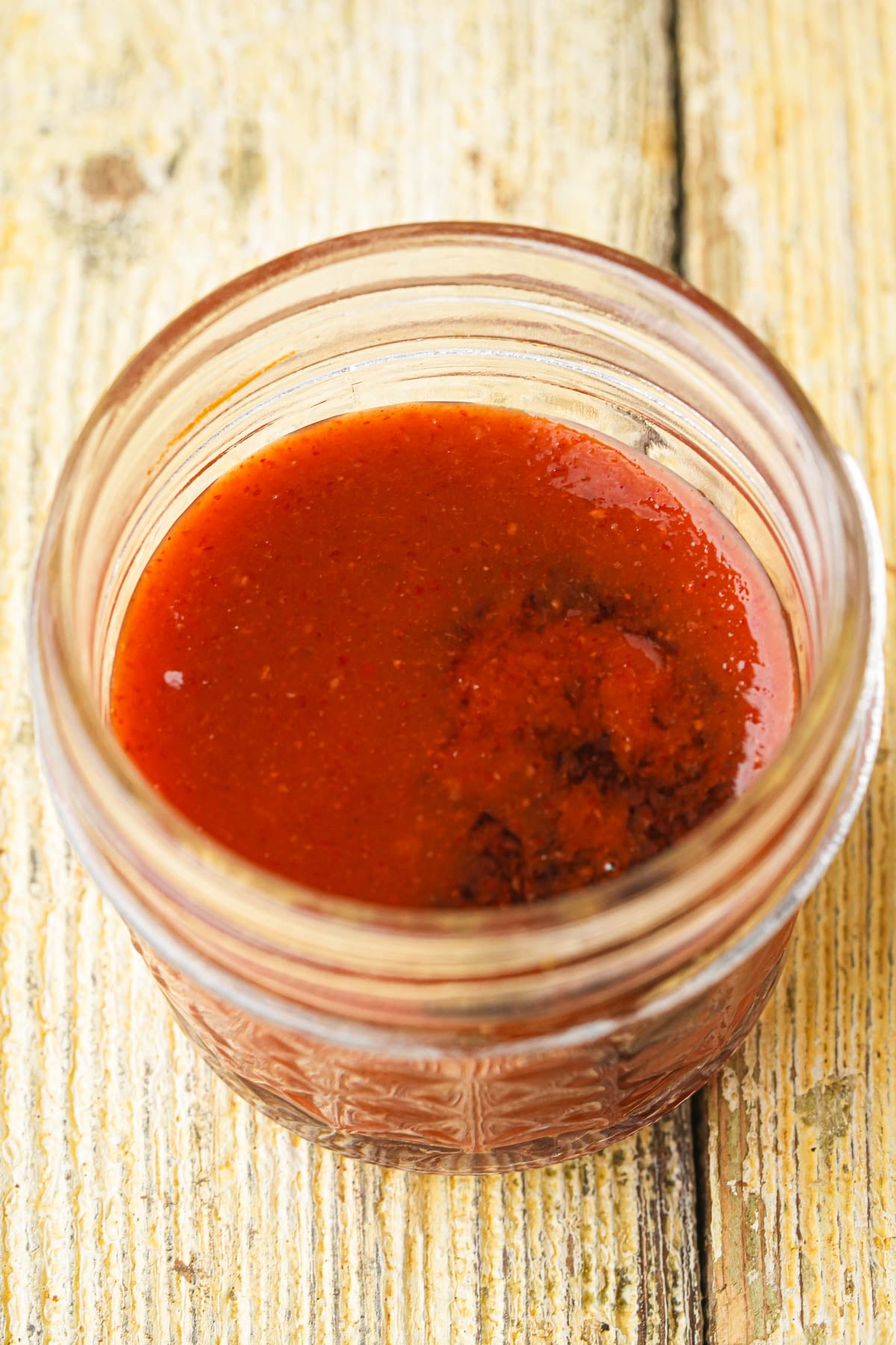 A small glass jar filled with gochujang and maple syrup sitting on a rustic wooden surface.