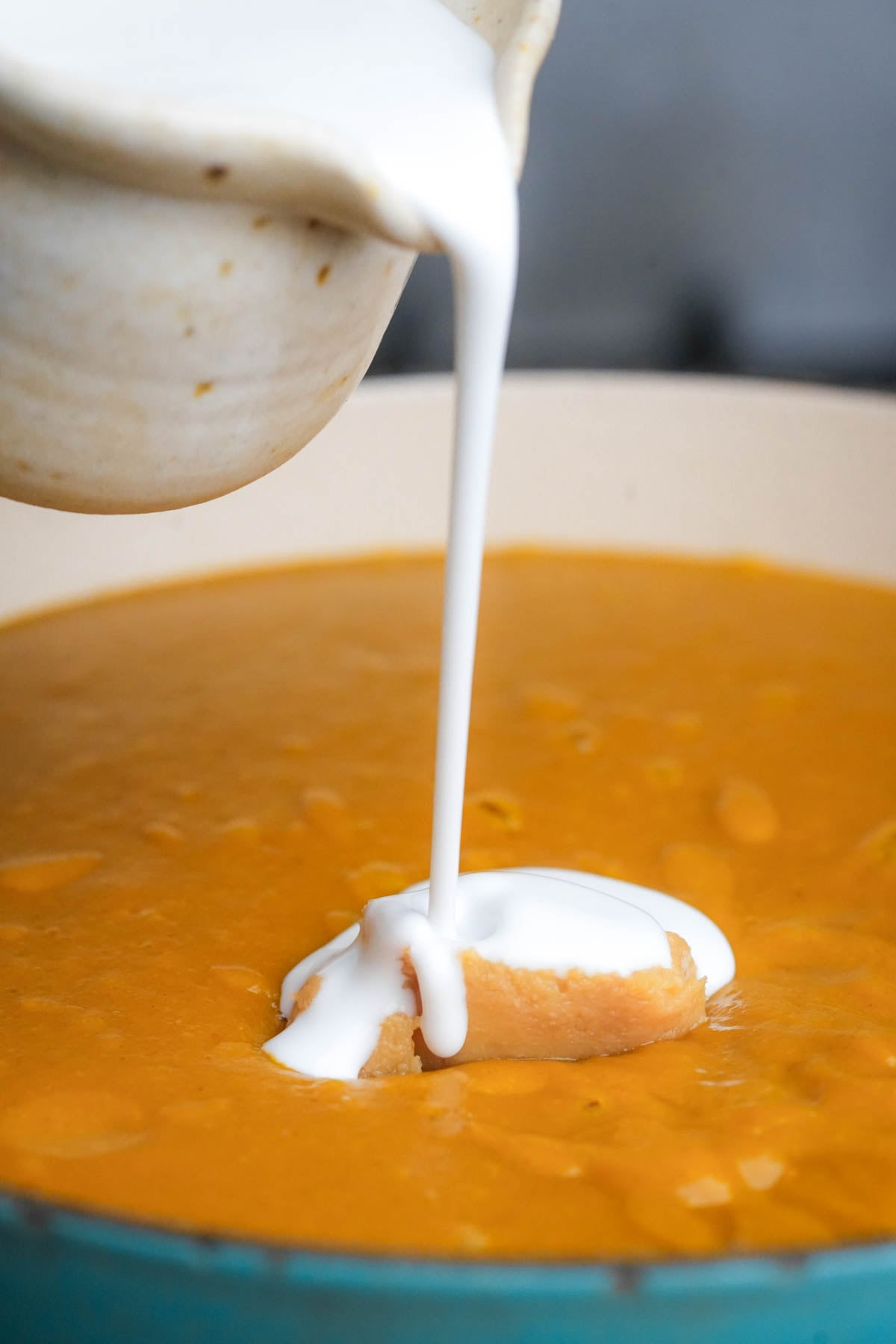 A bowl pours coconut milk onto a dollop of miso floating in a pot of kabocha squash soup.