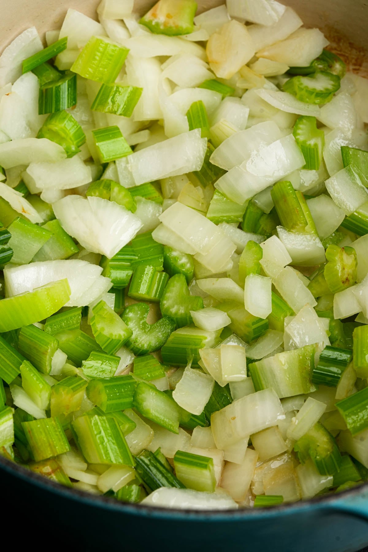 Chopped celery and onions being sautéed in a pot, with pieces turning translucent and slightly golden.