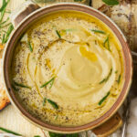 A bowl of vegan truffle cauliflower soup is garnished with olive oil, fresh rosemary, and black pepper.