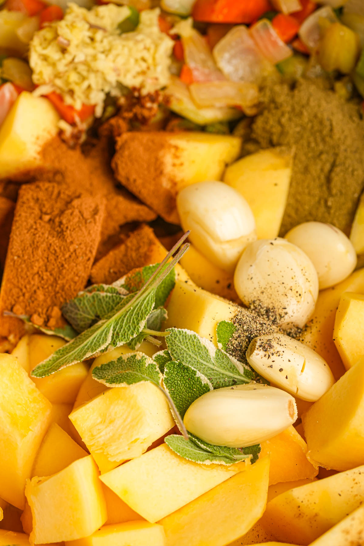 Chopped acorn squash, whole garlic cloves, fresh sage, ground spices, and diced vegetables being cooked.