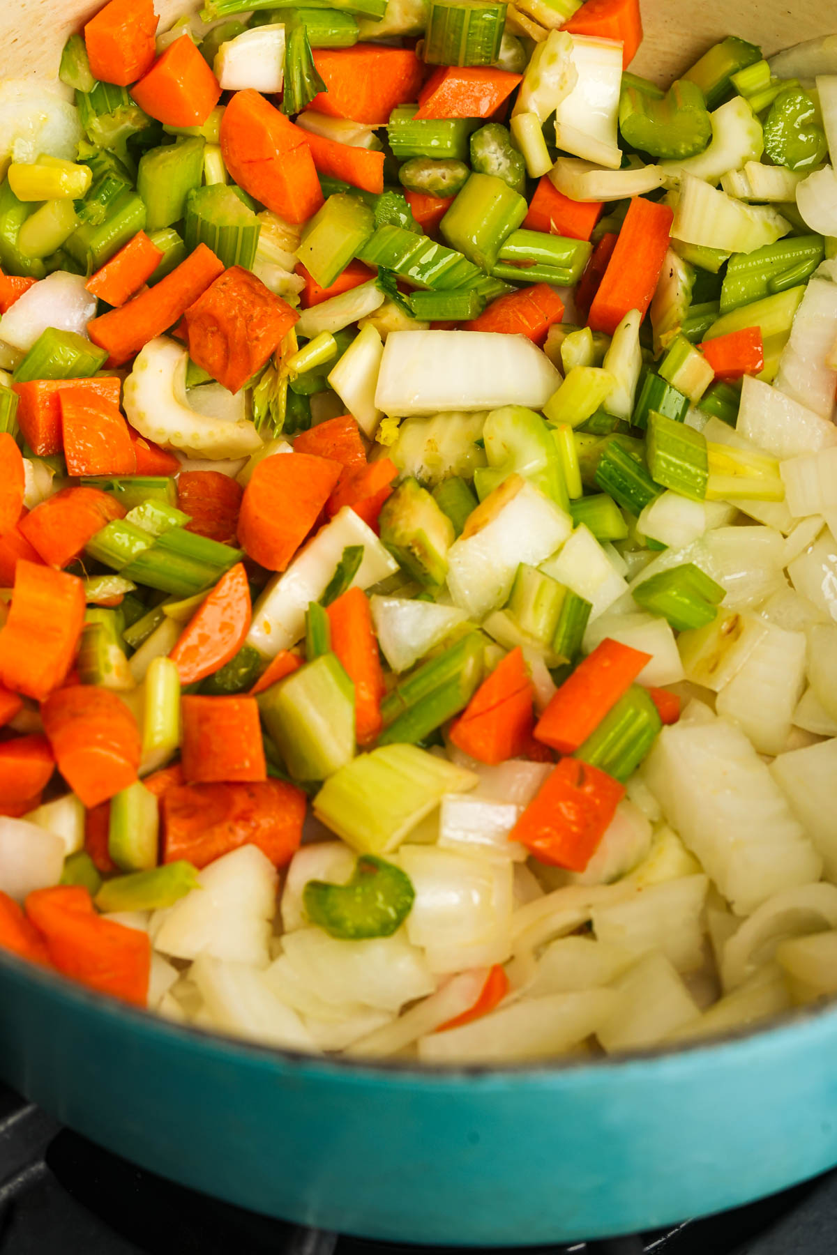 Chopped carrots, celery, and onions are being sautéed in a large blue pot on a stovetop.