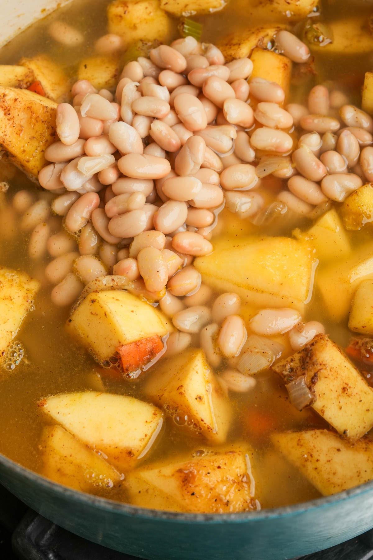 A pot filled with diced potatoes, acorn squash, white beans, and broth, being cooked together with visible spices.