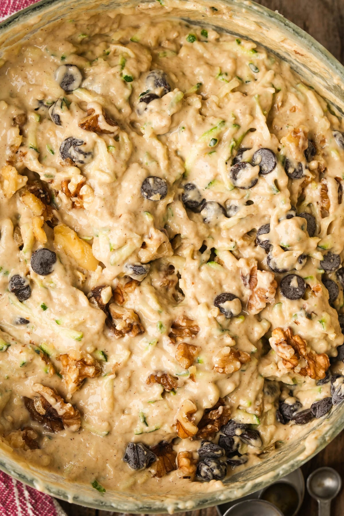 Close-up of vegan zucchini muffin batter mixed with chocolate chips and chopped walnuts in a bowl, ready to be baked.