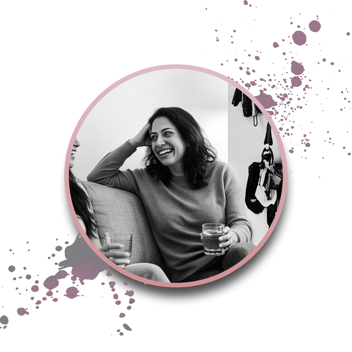 A woman sits on a couch, smiling and holding a drink. She is engaged in conversation with another person. The photo is black and white with a round pink border and paint splatter accents.