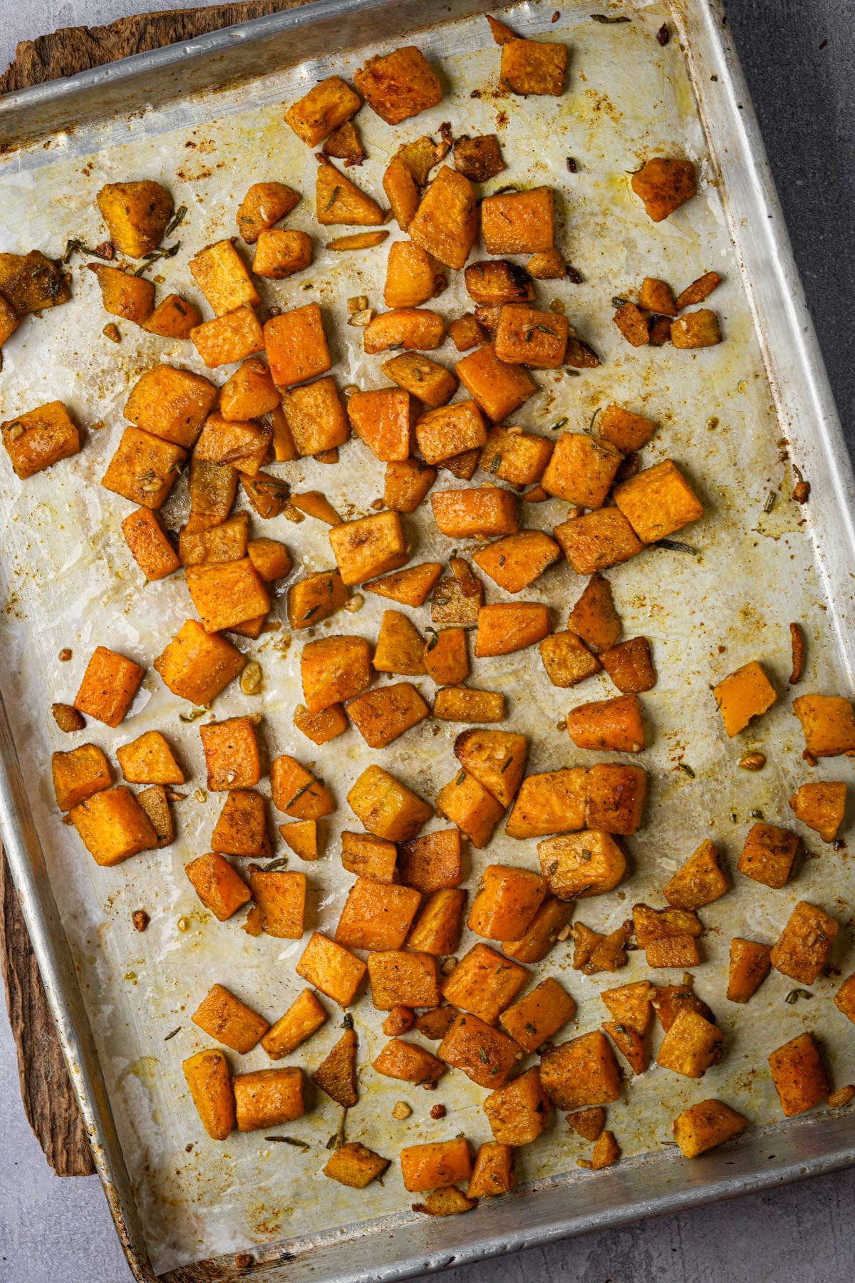 A baking sheet topped with roasted pumpkin cubes, seasoned and browned, spread out across the pan.