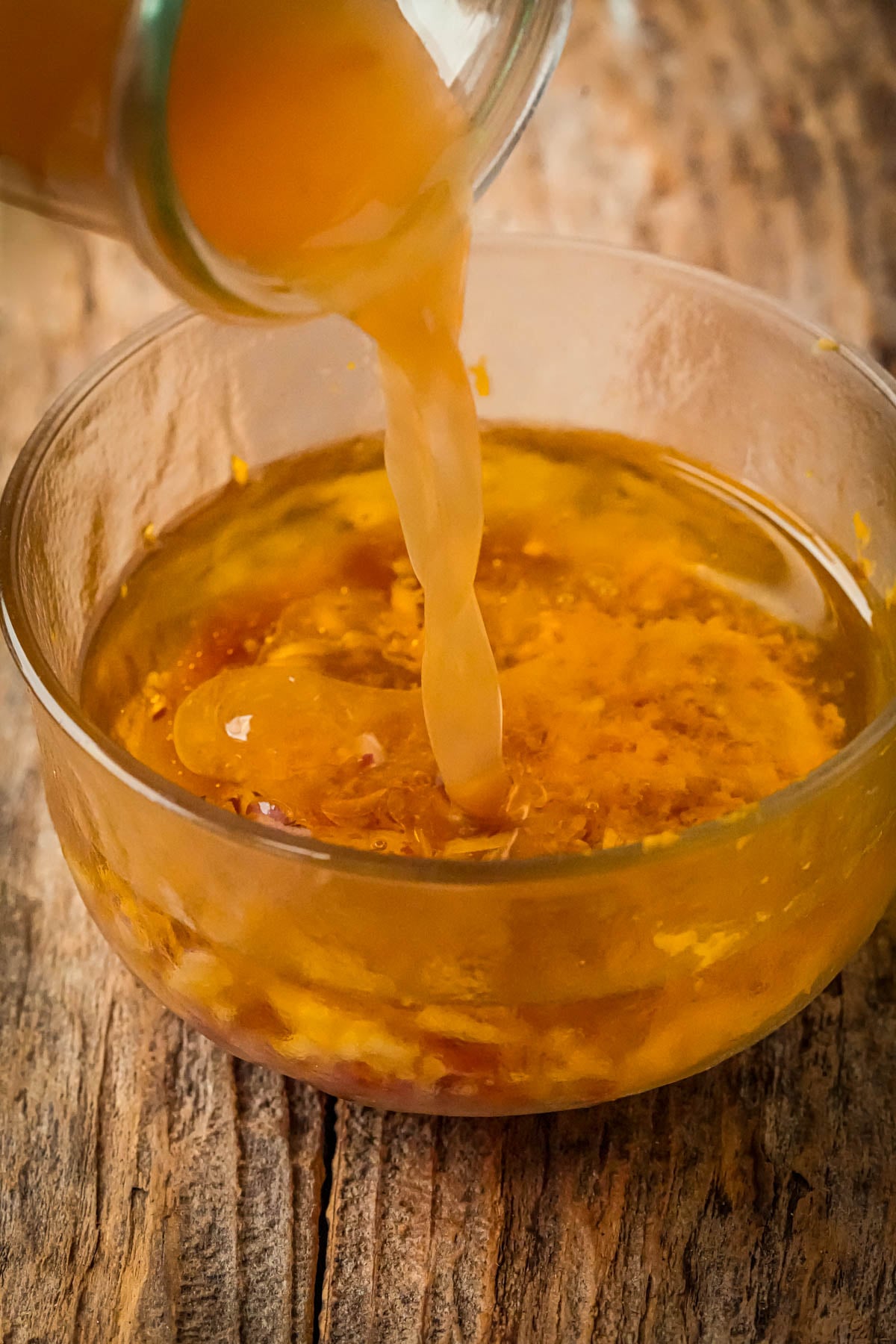 Apple cider liquid being poured from a jar into a glass bowl filled with roasted pumpkin salad dressing, sitting on a rustic wooden surface.