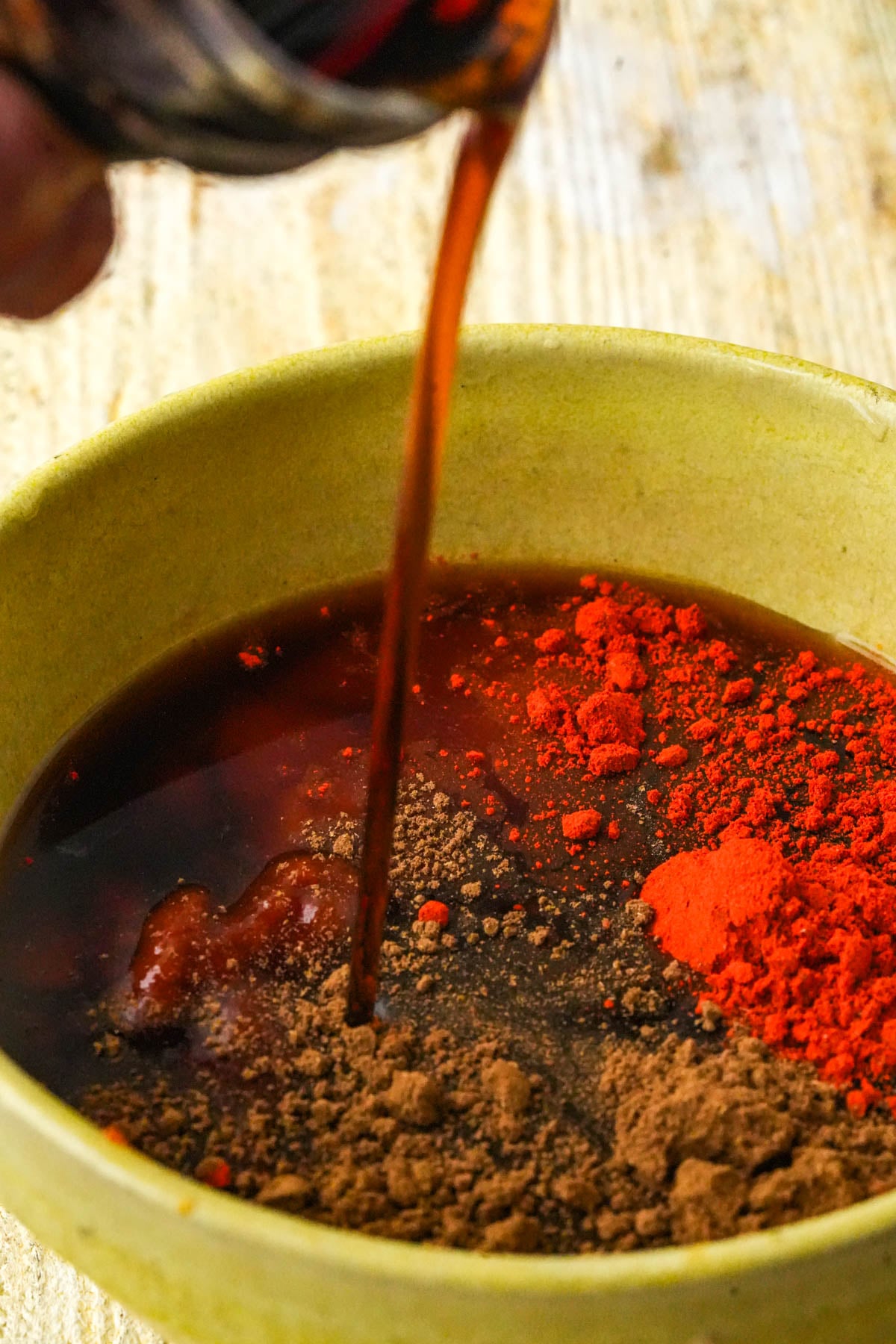 Rib glaze liquids poured into a bowl over Chinese 5-spice and annatto powder, ready to whisk.