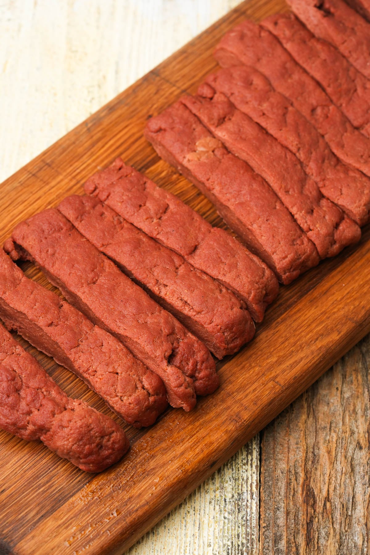 Seitan slab for vegan Chinese ribs cut into rib-sized strips on a wooden board.