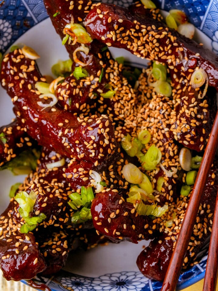 Vegan Chinese ribs coated in a red hoisin sriracha glaze, topped with toasted sesame seeds and scallions.