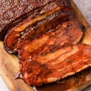 Slices of glazed, herb-crusted vegan bbq brisket on a wooden cutting board.