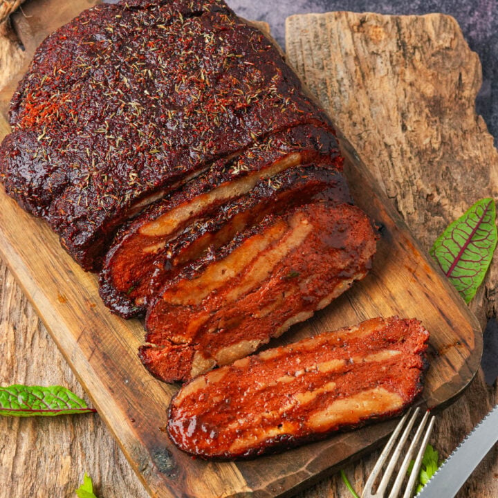 Sliced vegan bbq brisket on a wooden cutting board with a fork and knife.