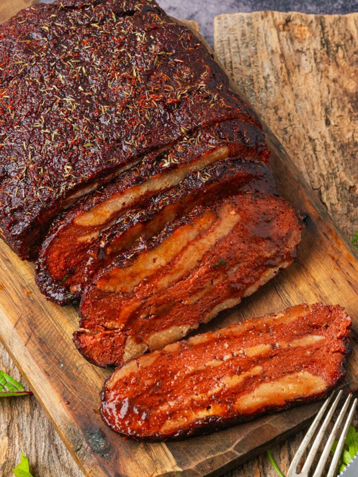Sliced vegan bbq brisket on a wooden cutting board with a fork and knife.