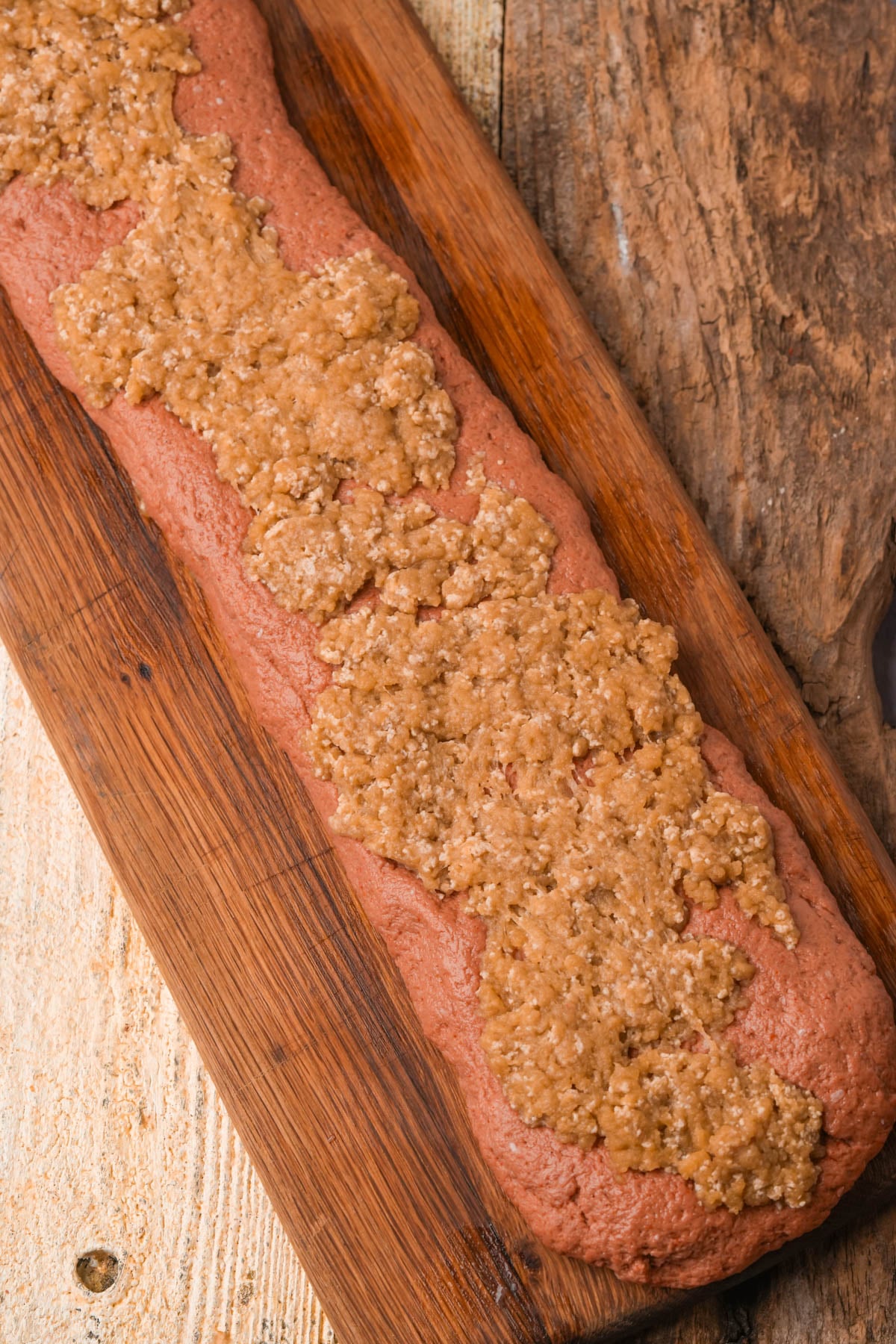 Pink seitan meat dough topped with a layer of fat dough on a wooden board.