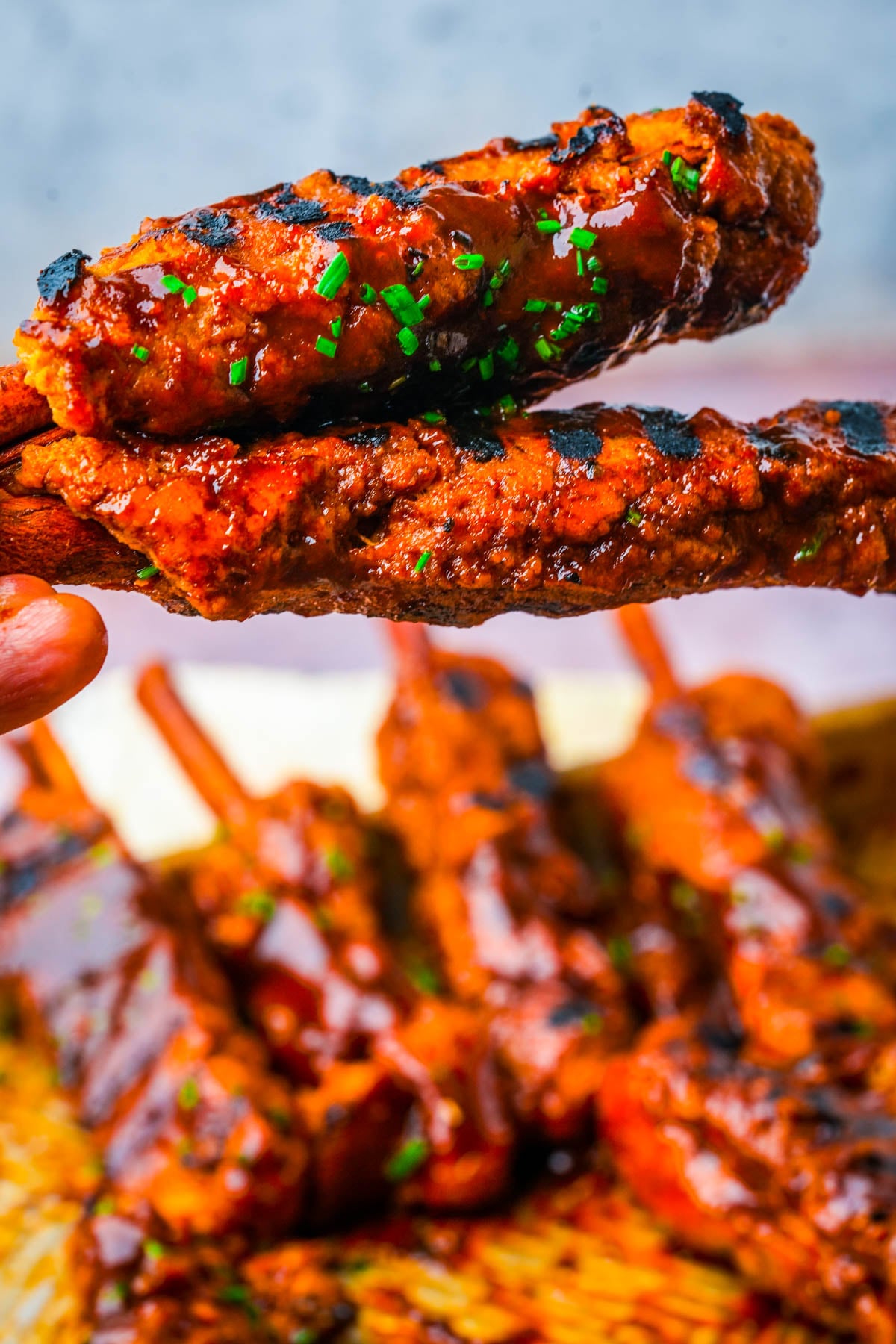 Vegan BBQ ribs with charred grill marks and chives, held up by their cinnamon stick bones.