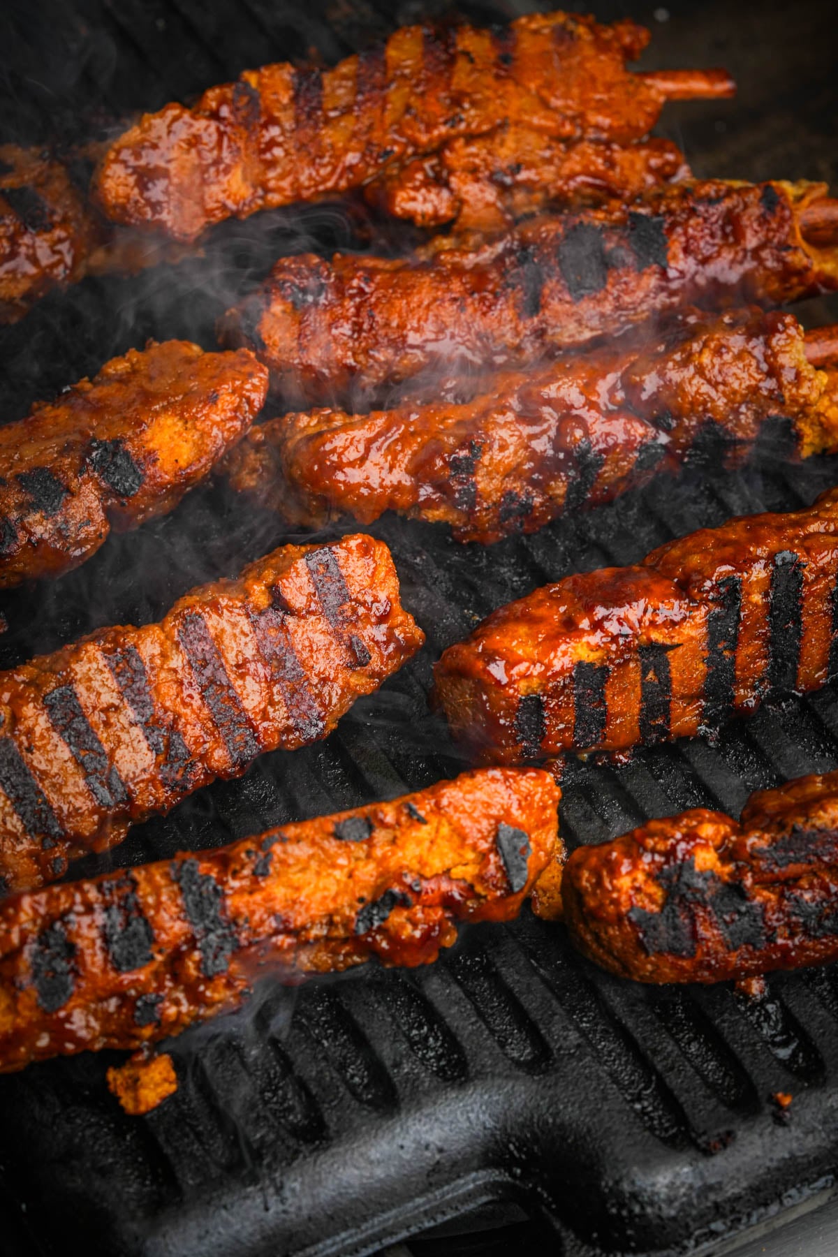 Vegan BBQ ribs brushed with sauce and charring on a hot grill pan.